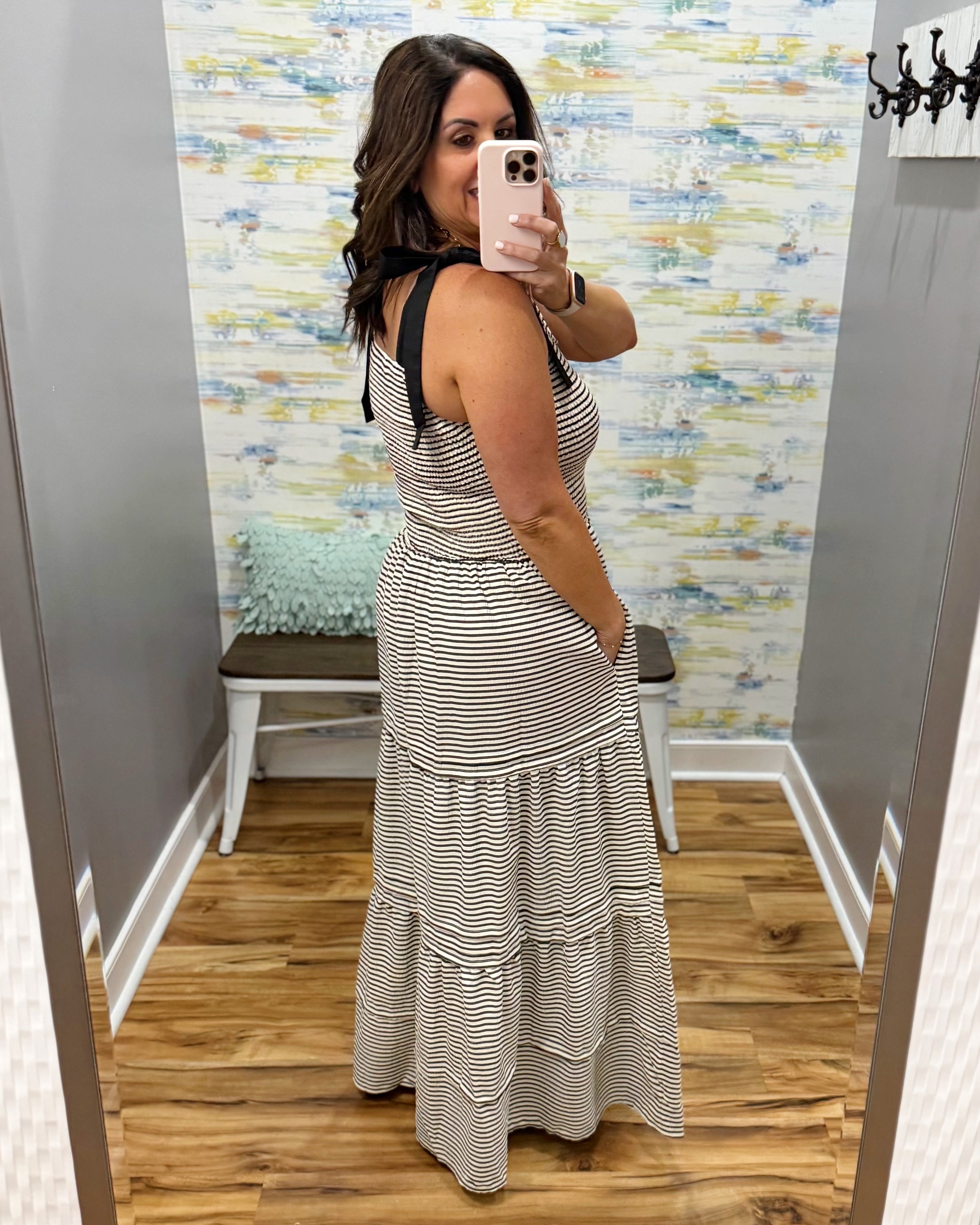 Woman taking a mirror selfie wearing a striped dress in a fitting room.