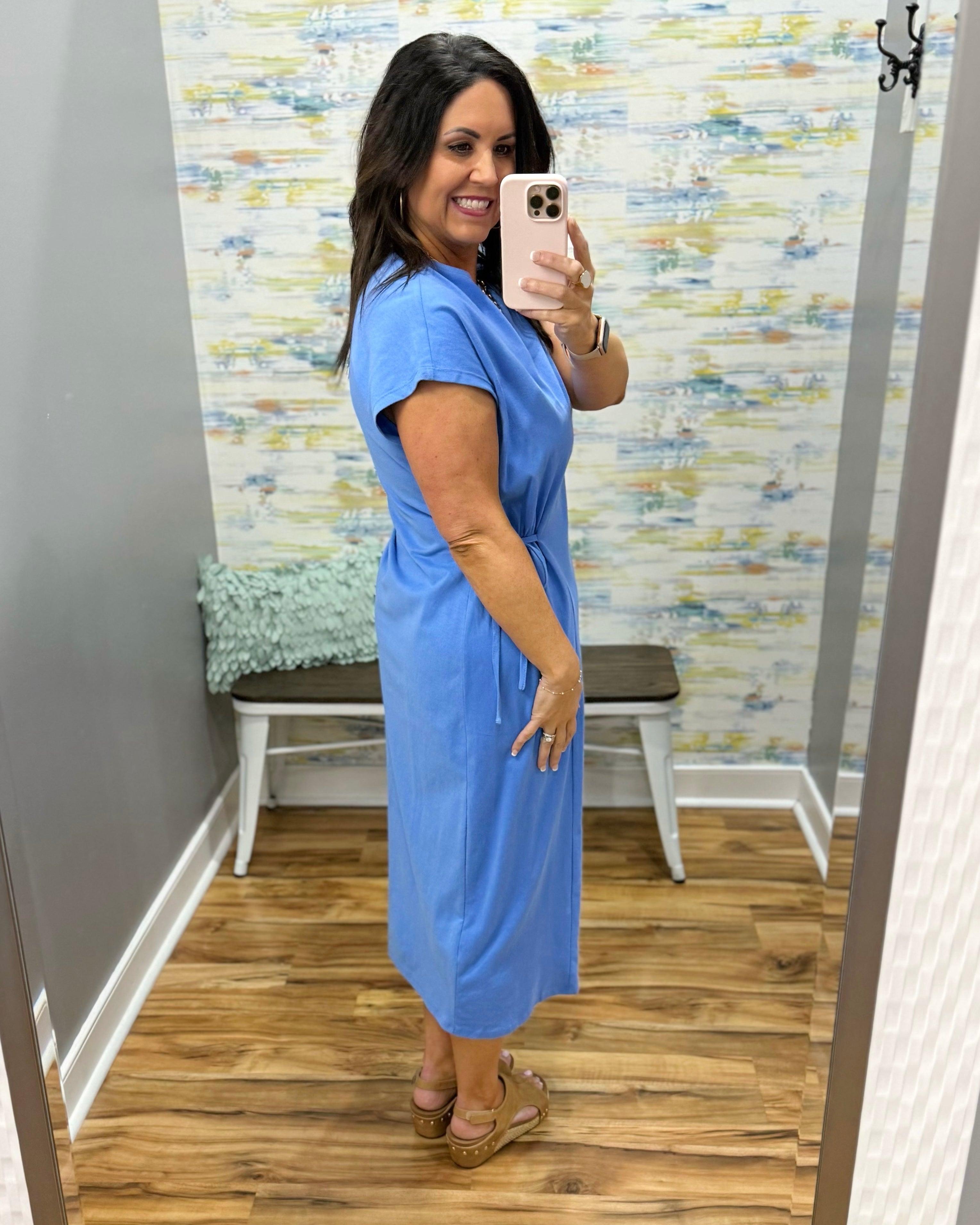 Woman wearing a blue dress in a room with patterned wallpaper.