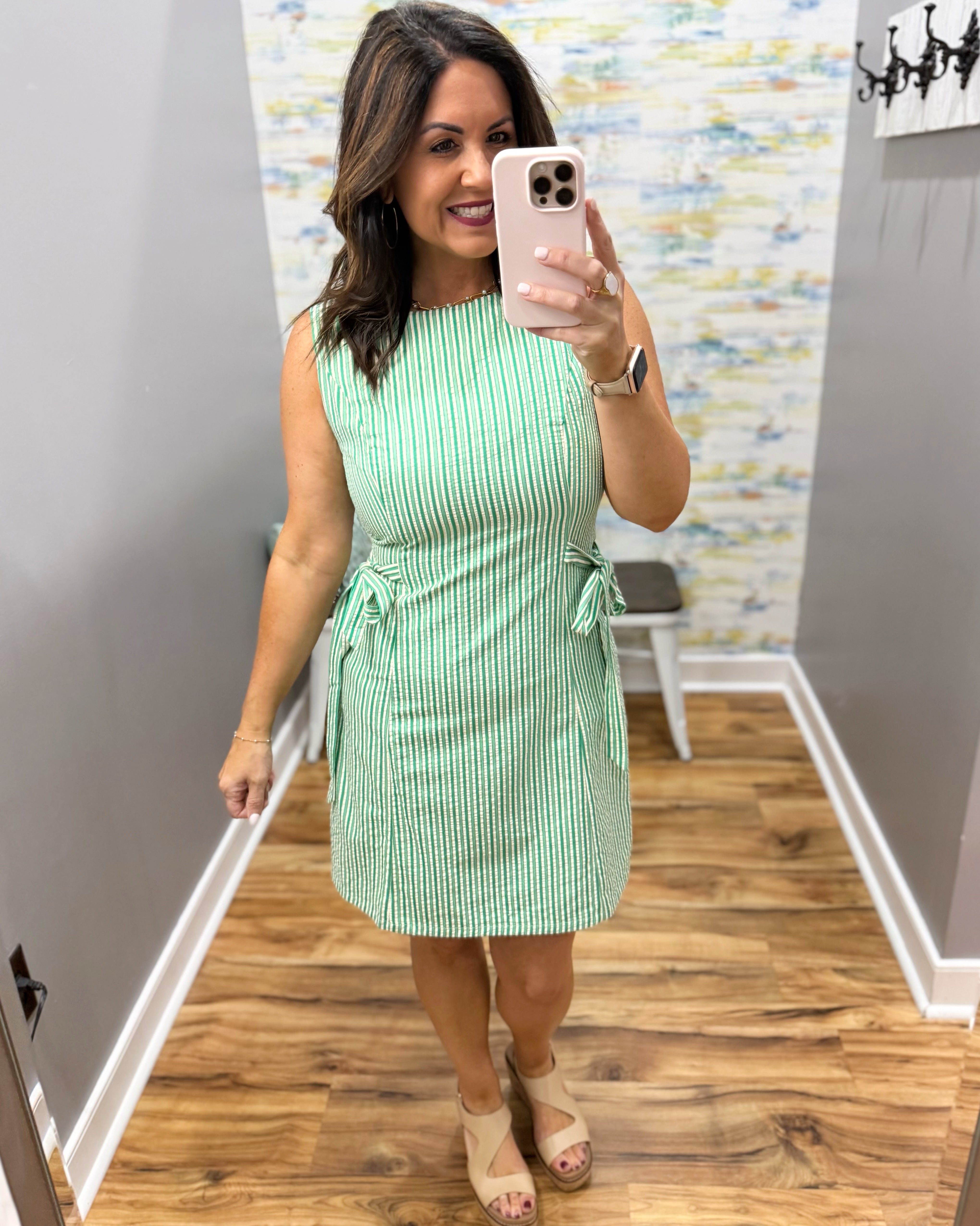 Woman taking a mirror selfie wearing a green striped dress in a room with a colorful wall.