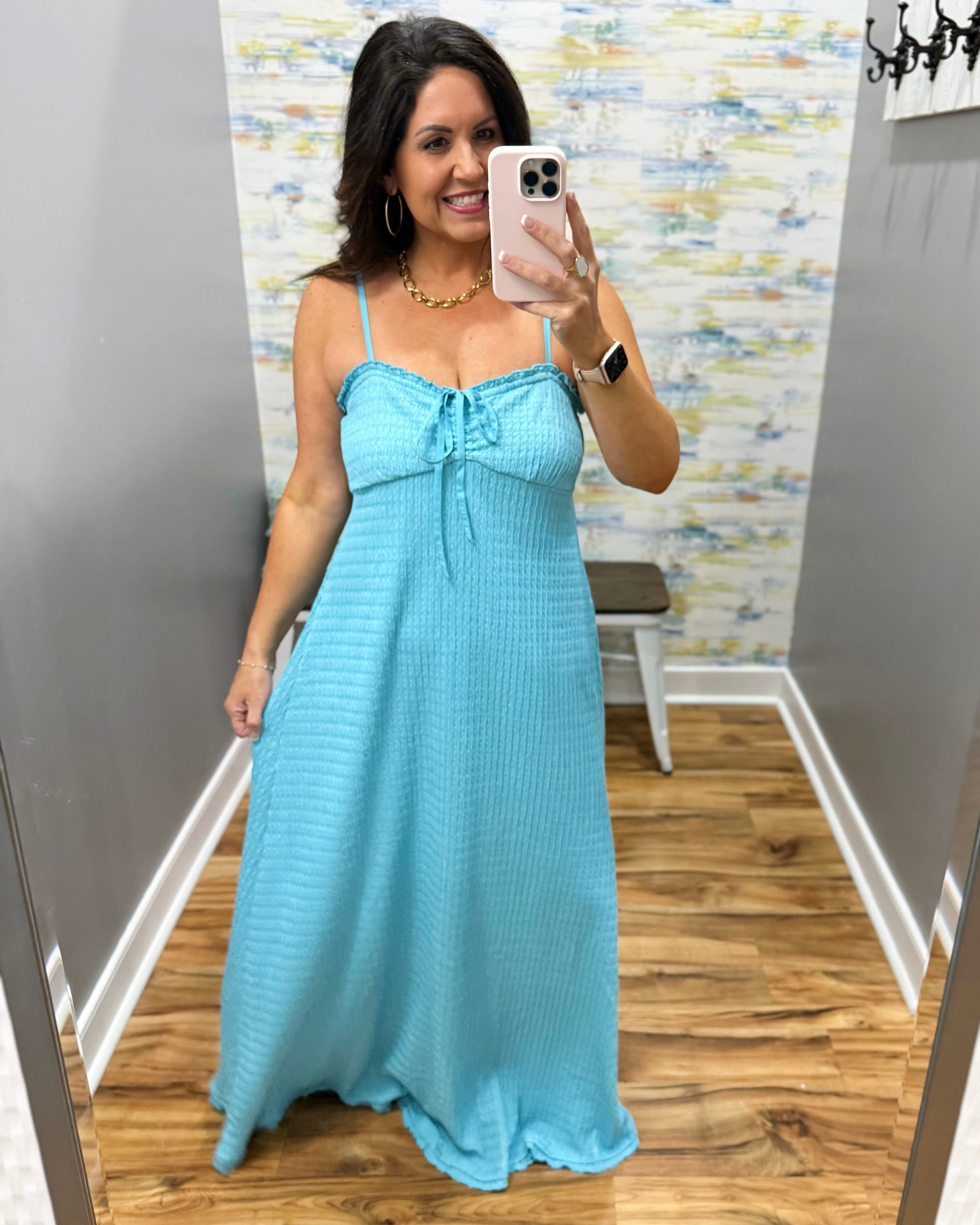 Woman taking a mirror selfie wearing a light blue dress in a room with a patterned wall.
