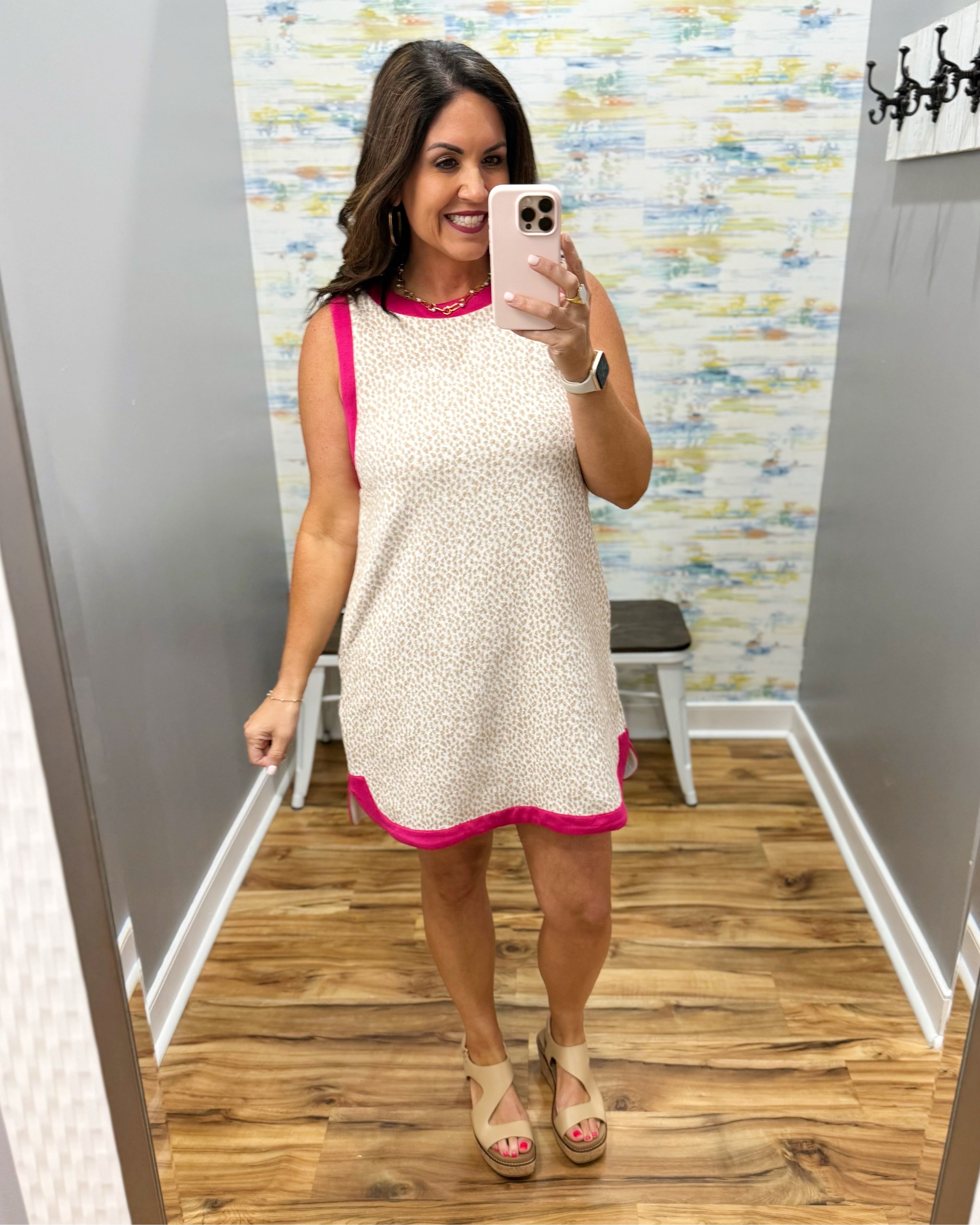 Woman taking a mirror selfie wearing a beige dress with pink trim in a store.