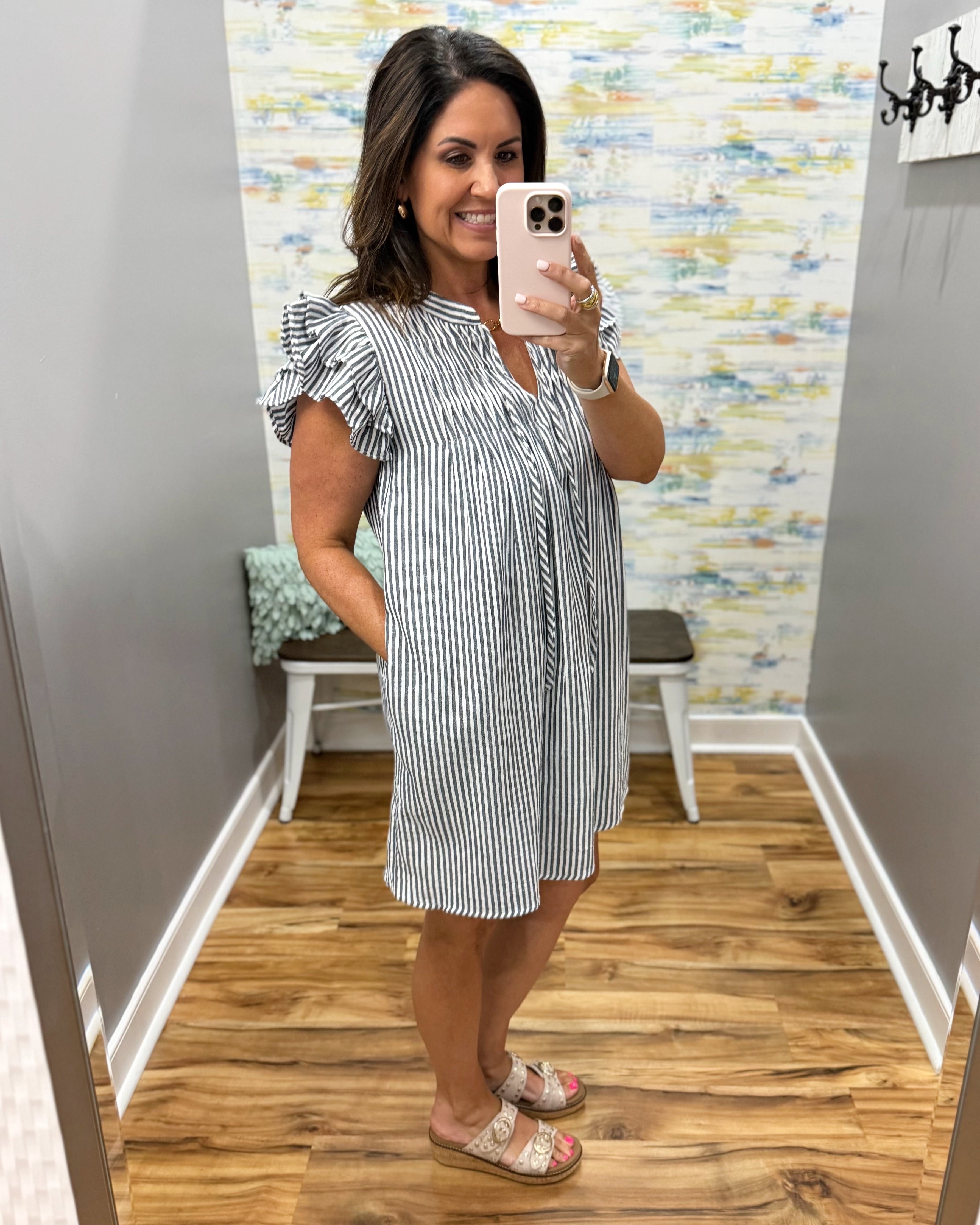 Woman taking a mirror selfie wearing a black and white striped dress in a room with a patterned wall.
