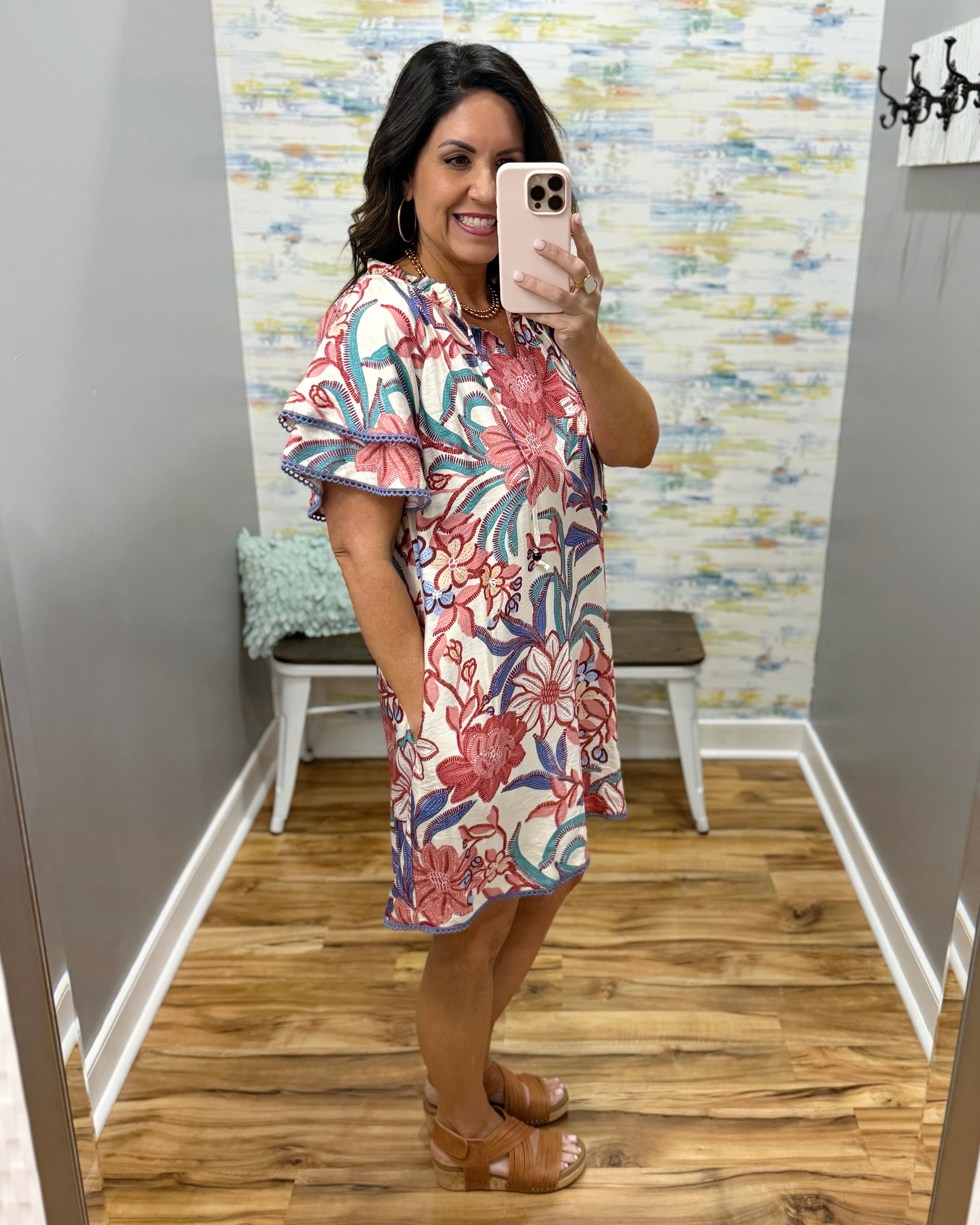 Woman taking a mirror selfie wearing a floral dress in a room with a colorful wall.