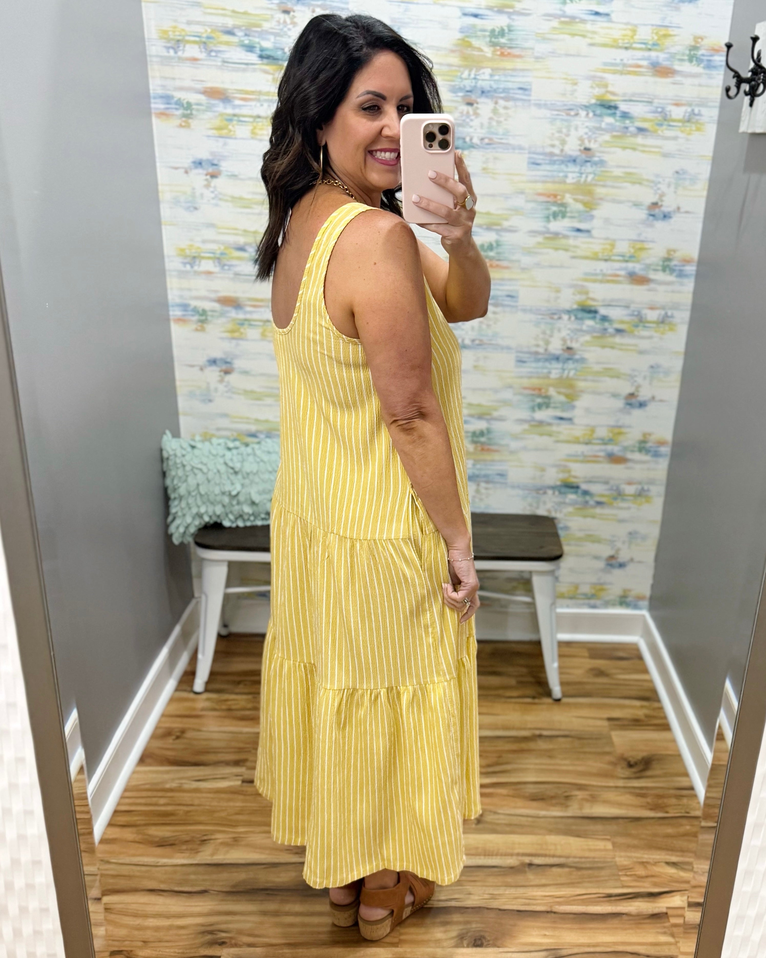 Woman wearing a yellow dress taking a mirror selfie in a room with a textured wall.