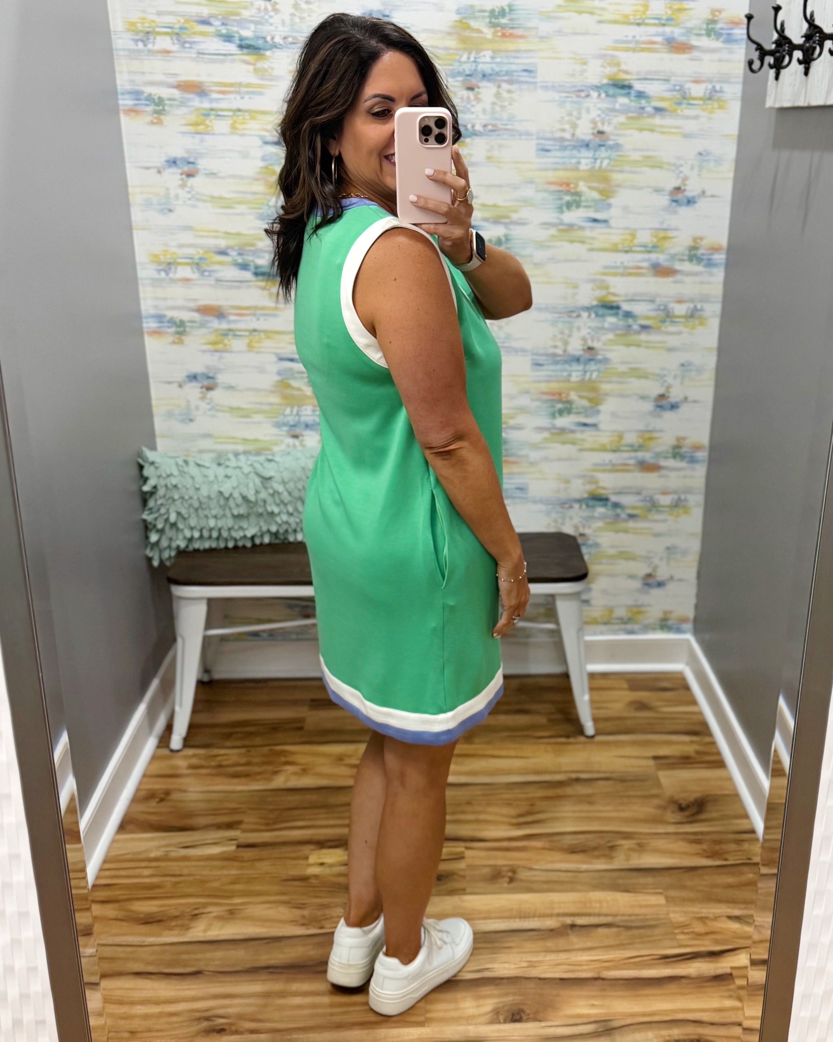 Woman taking a mirror selfie wearing a green dress in a room with a textured wall and wooden floor.