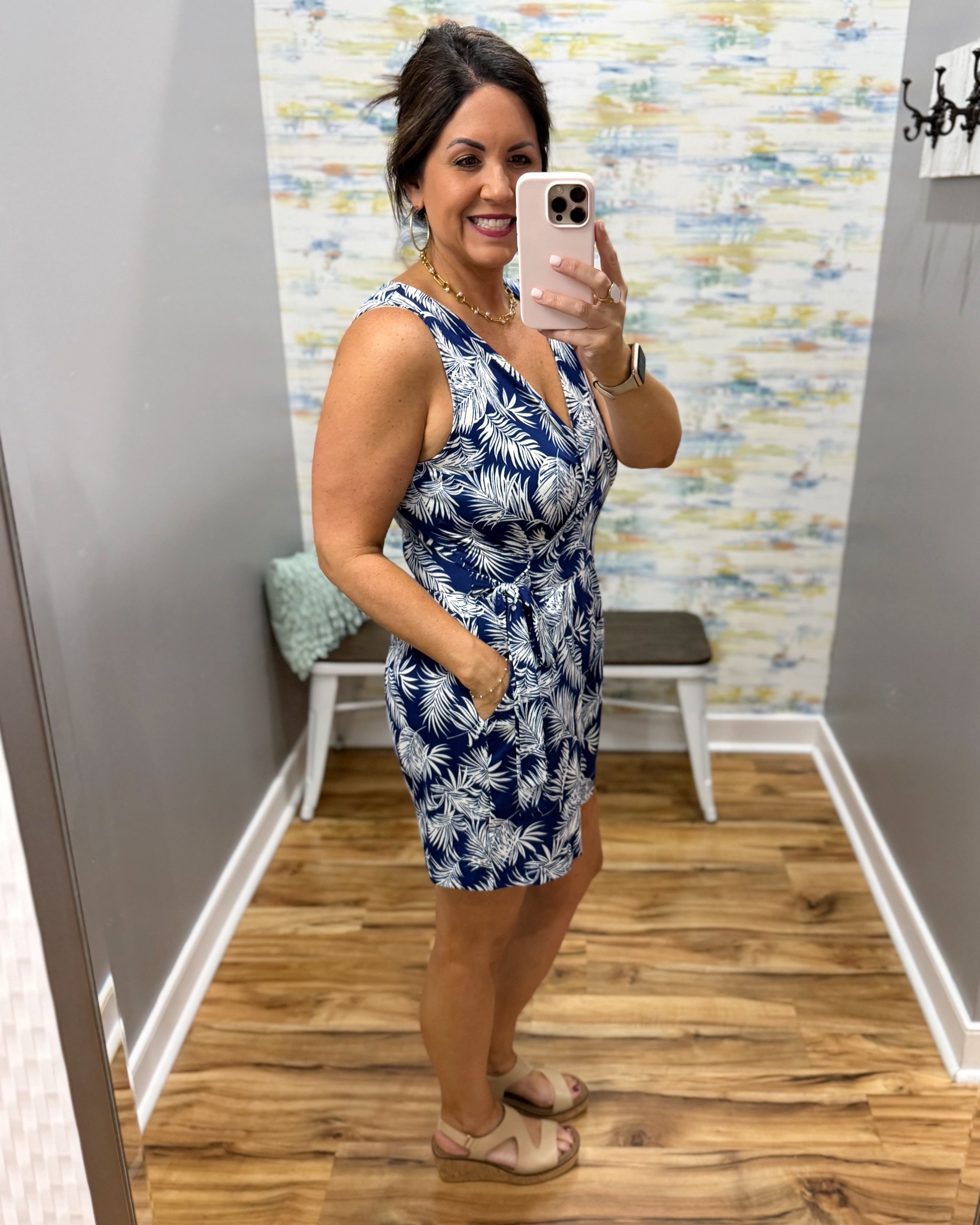 Woman taking a mirror selfie wearing a blue floral dress in a room with colorful wallpaper.