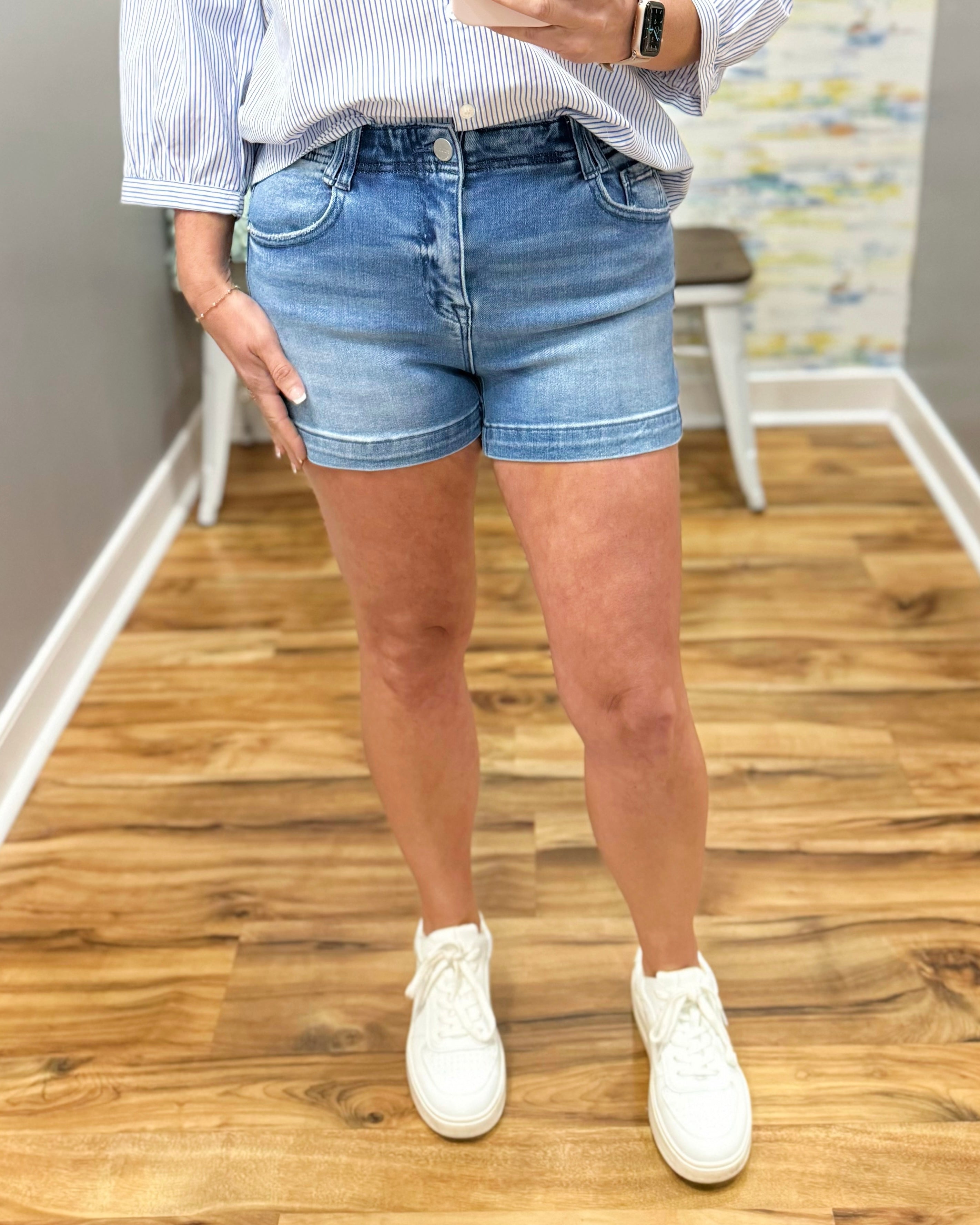 Person wearing denim shorts and white sneakers on a wooden floor.