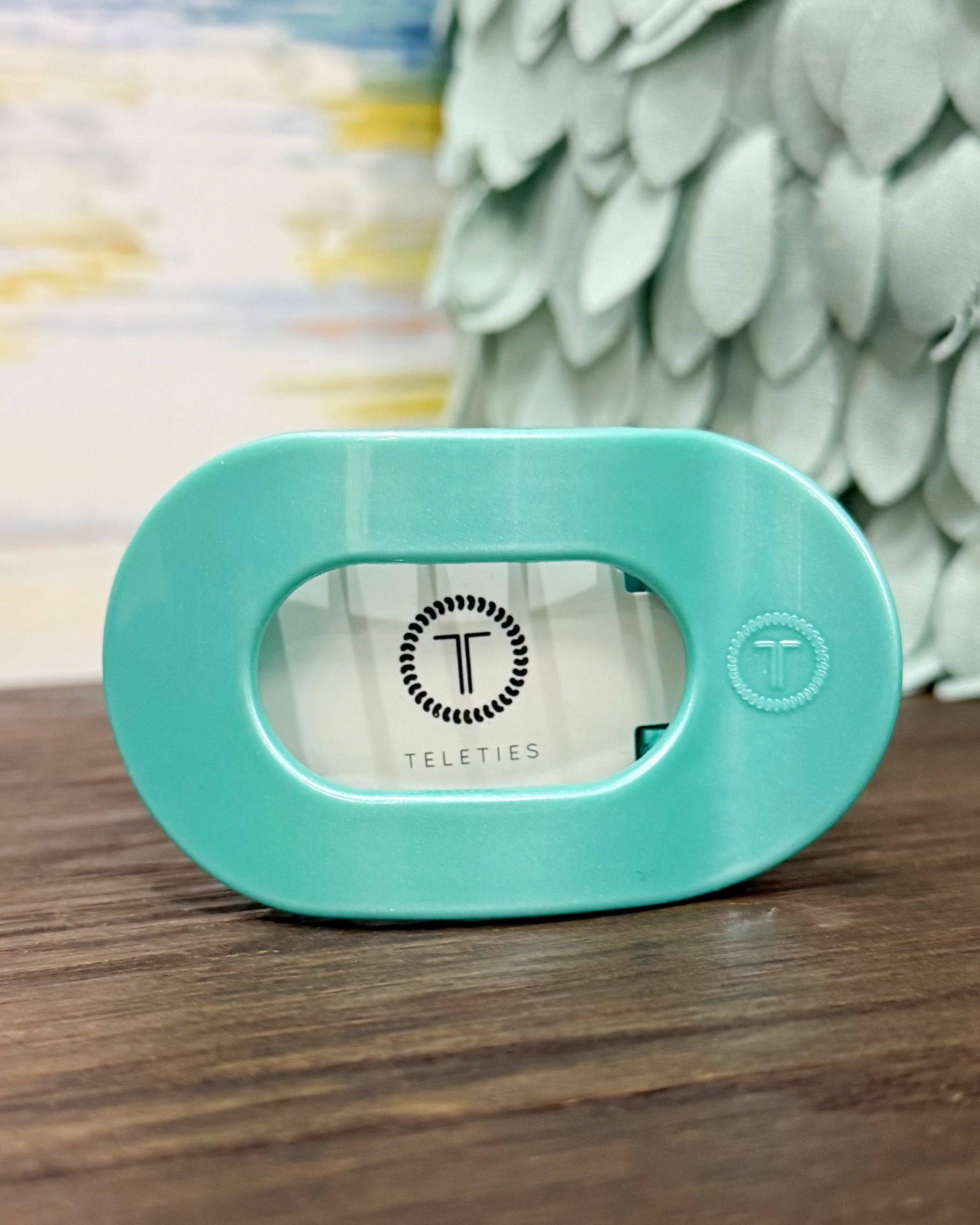 Turquoise hair claw with 'Teleties' branding on a wooden surface.