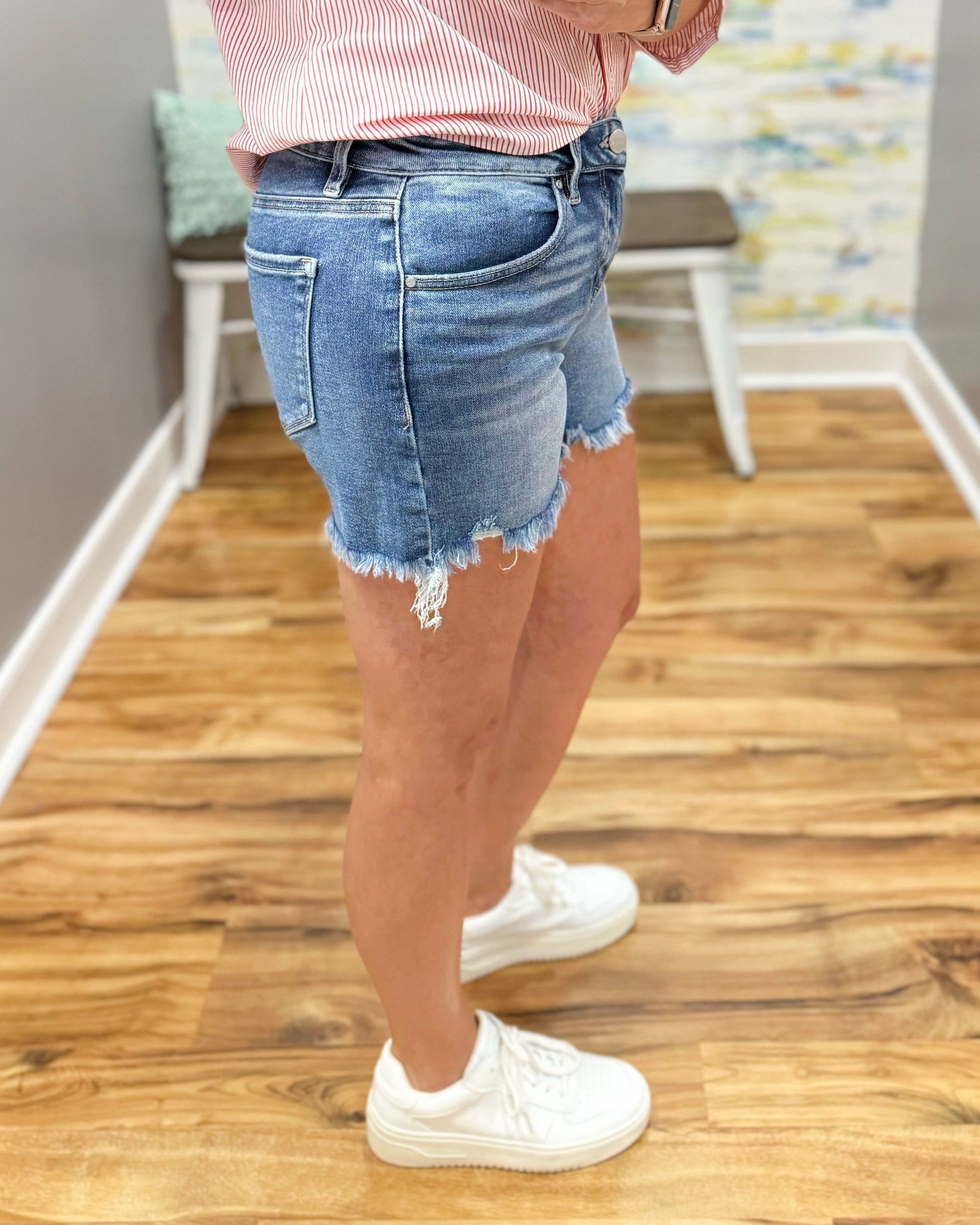 Person wearing denim shorts and white sneakers on a wooden floor.