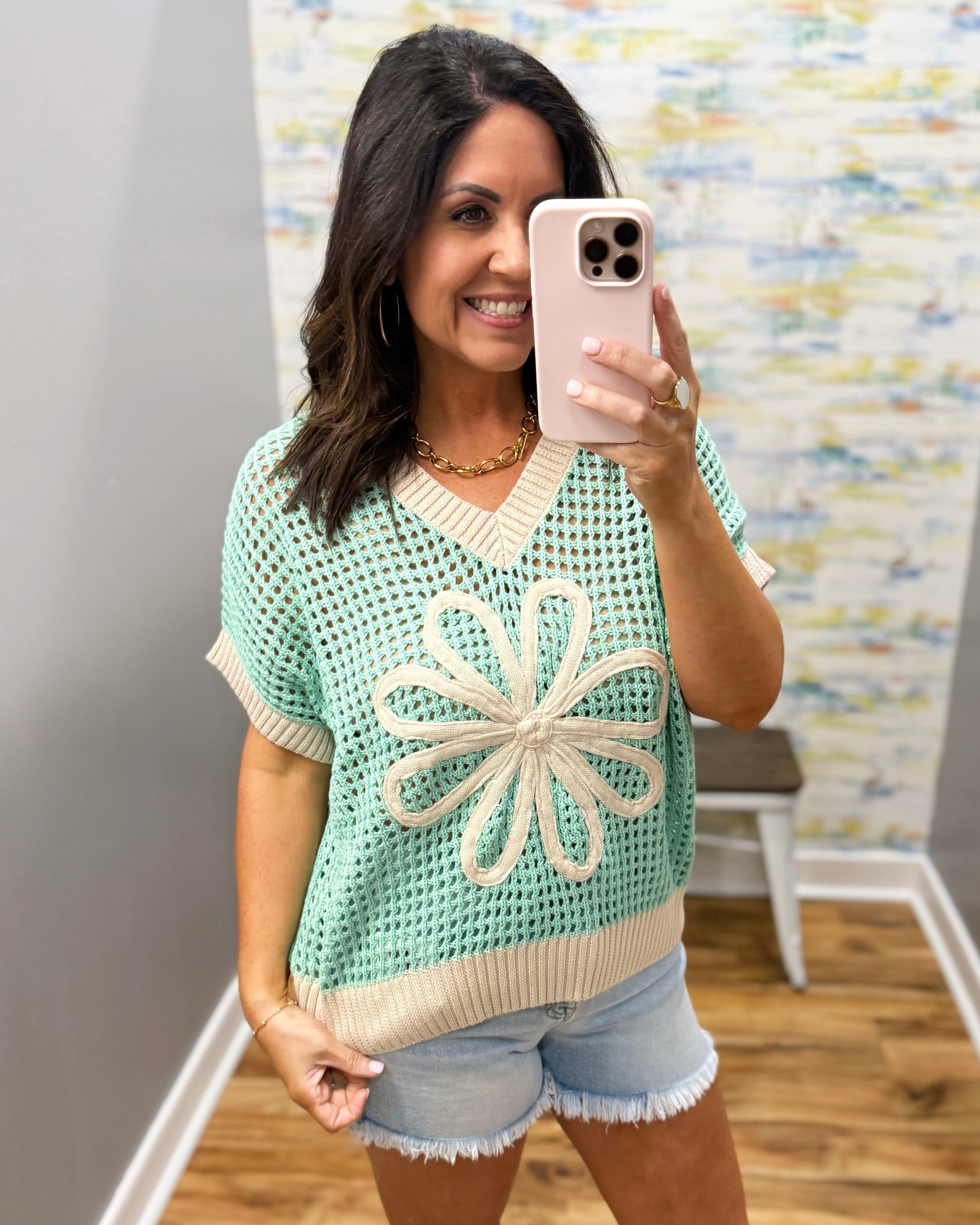 Woman taking a mirror selfie wearing a light blue crochet top with a flower design.