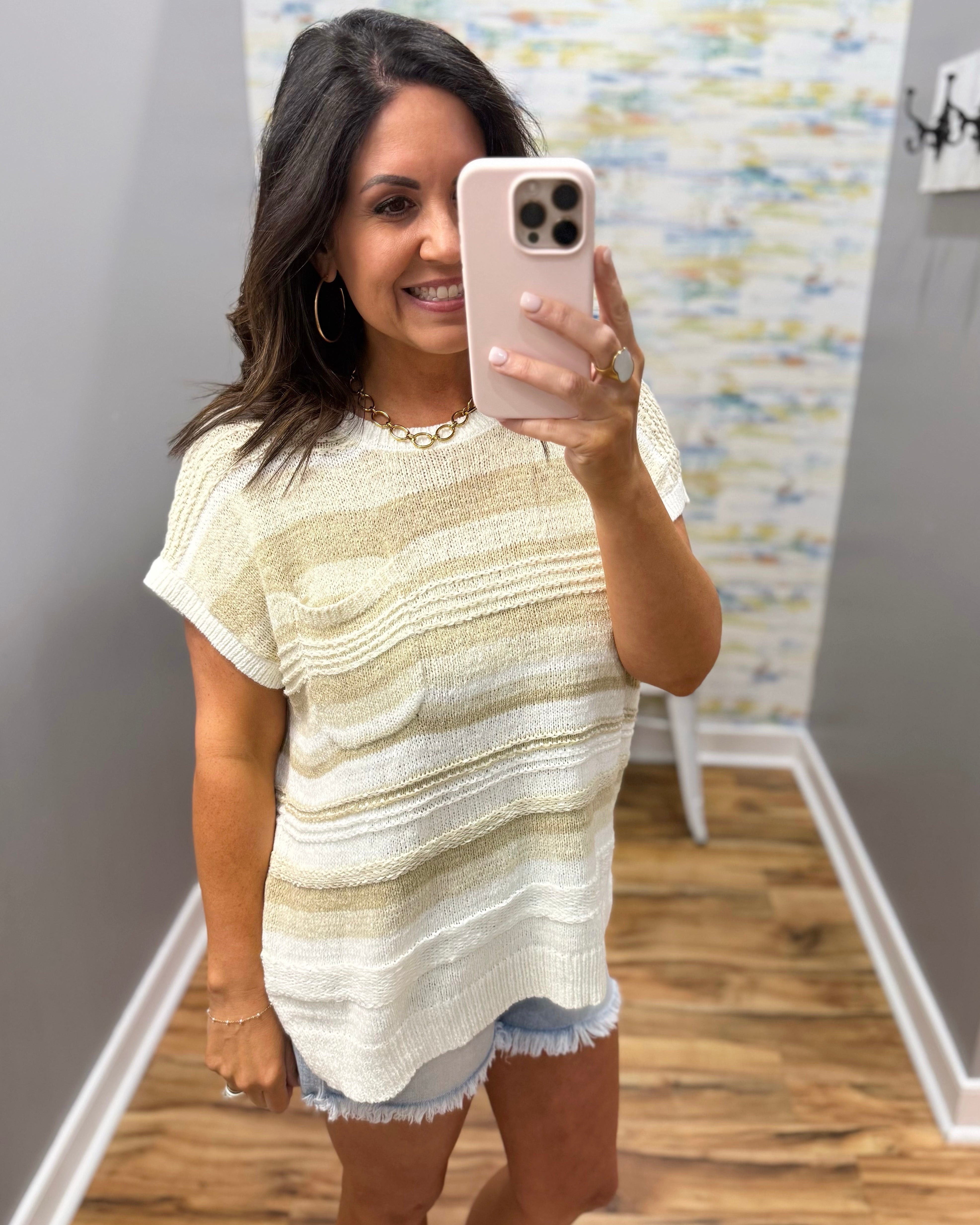 Woman taking a mirror selfie wearing a striped dress in a room with a patterned wall.