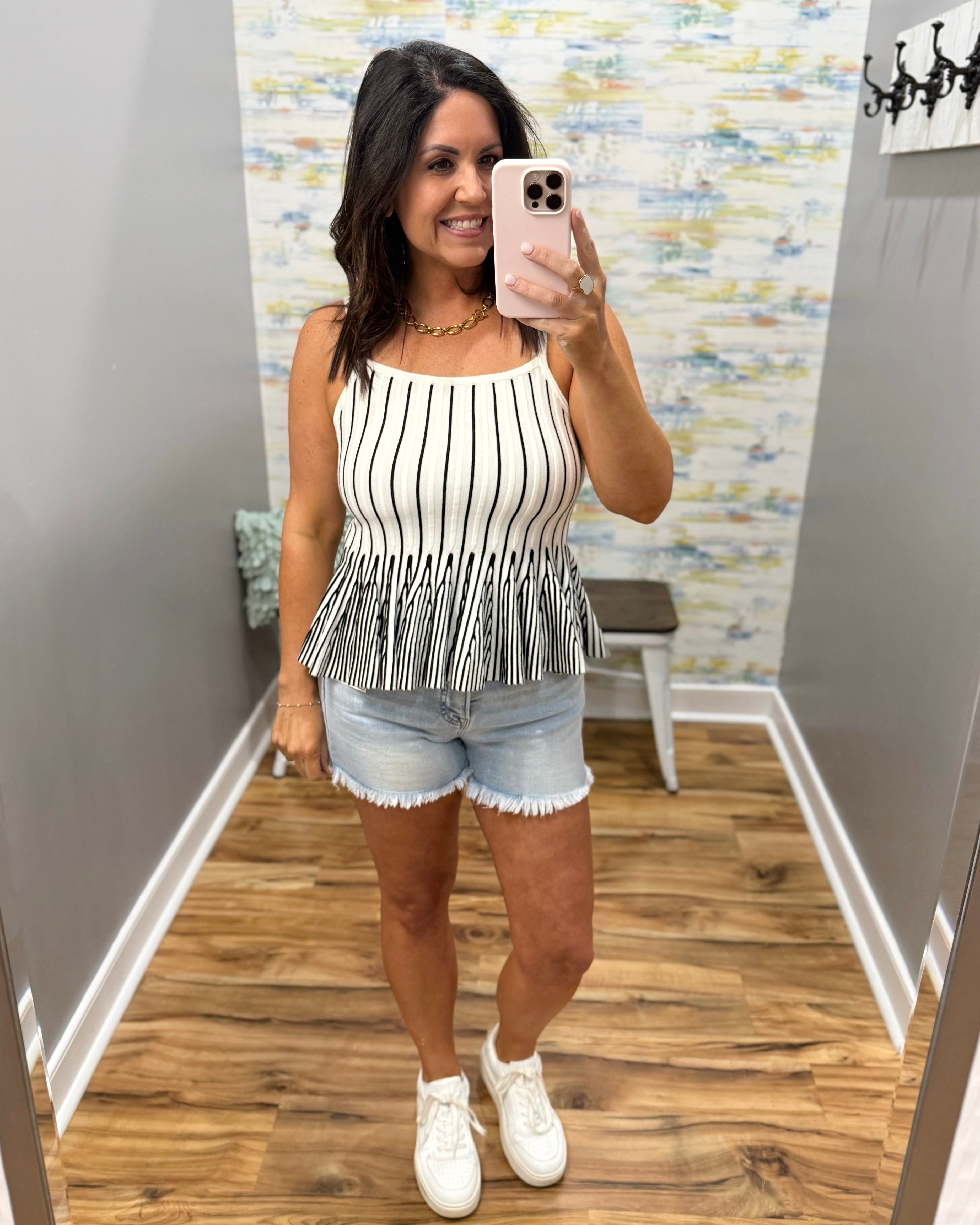 Woman taking a mirror selfie wearing a black and white striped peplum top and denim shorts.