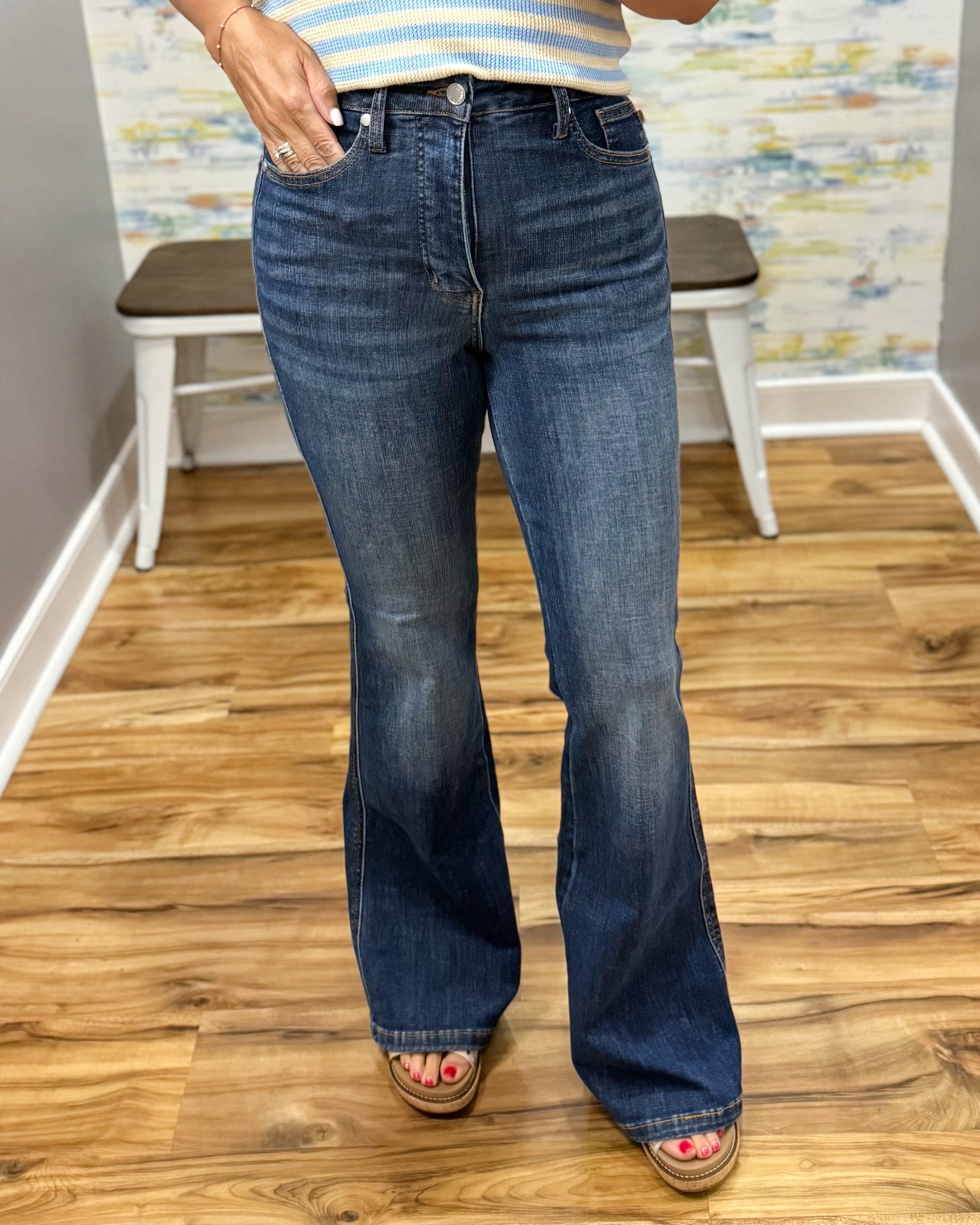 Person wearing blue flared jeans on a wooden floor with a colorful wall in the background