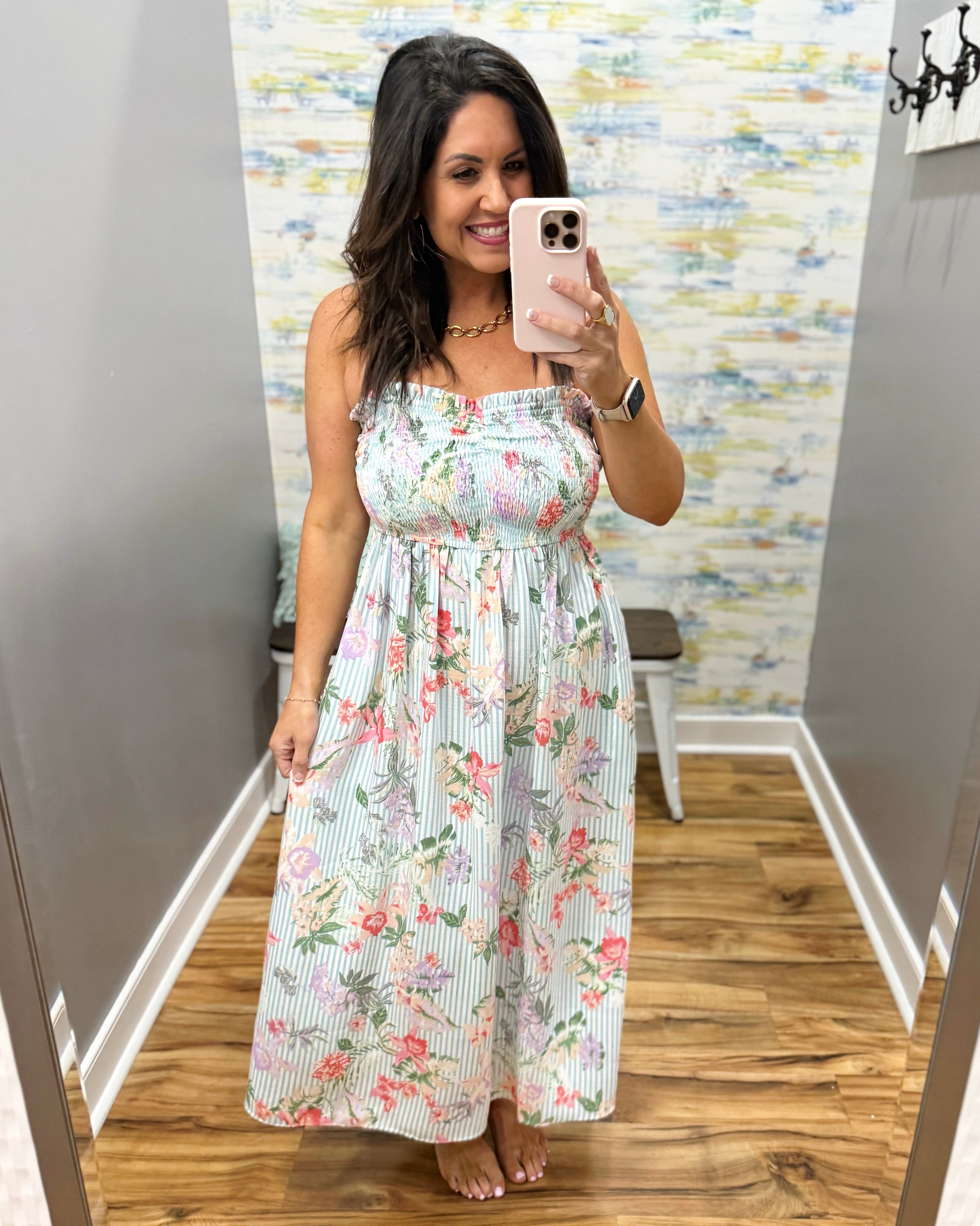 Woman taking a mirror selfie wearing a floral dress in a room with a patterned wall.