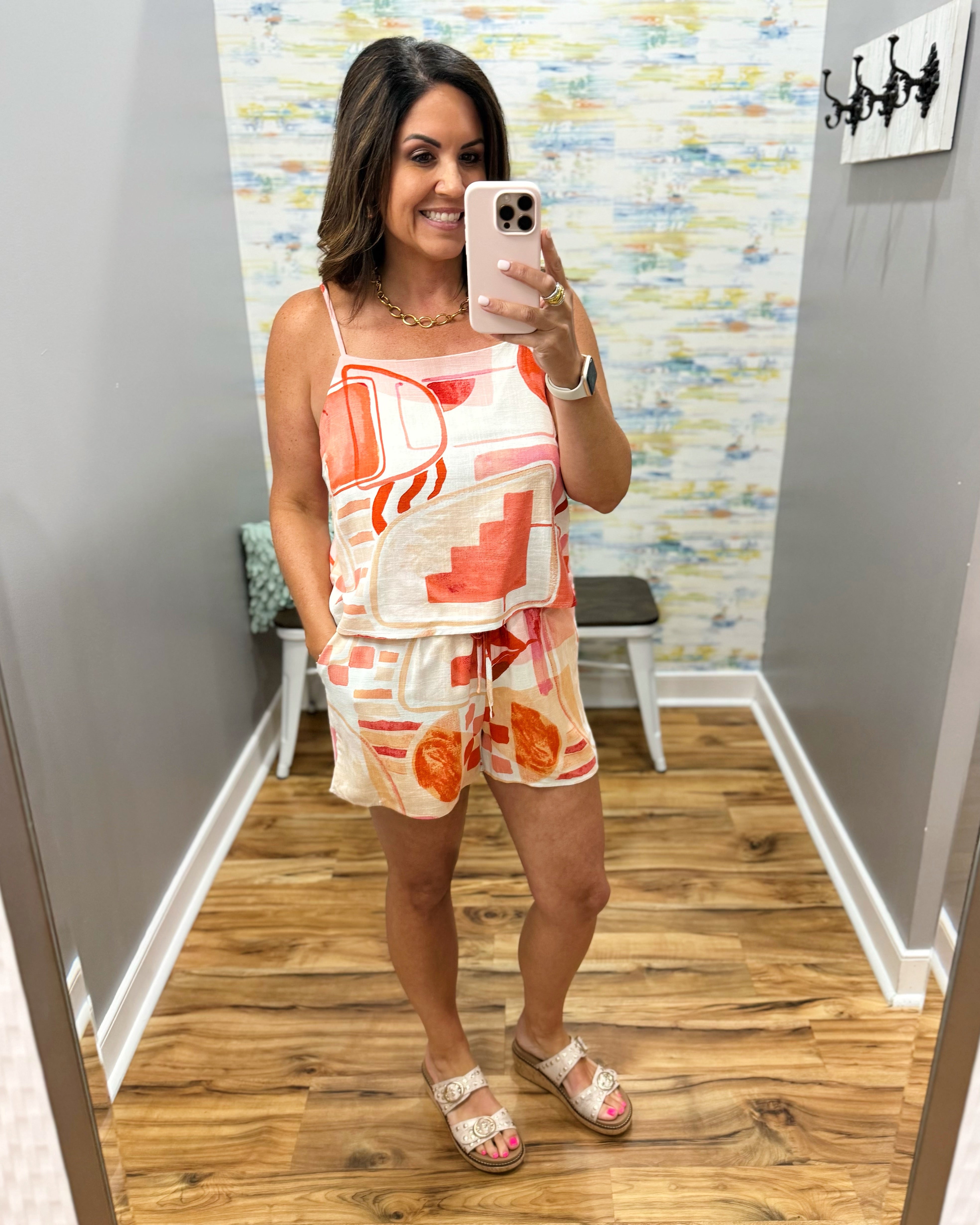 Woman taking a mirror selfie wearing a colorful outfit in a room with patterned wallpaper.