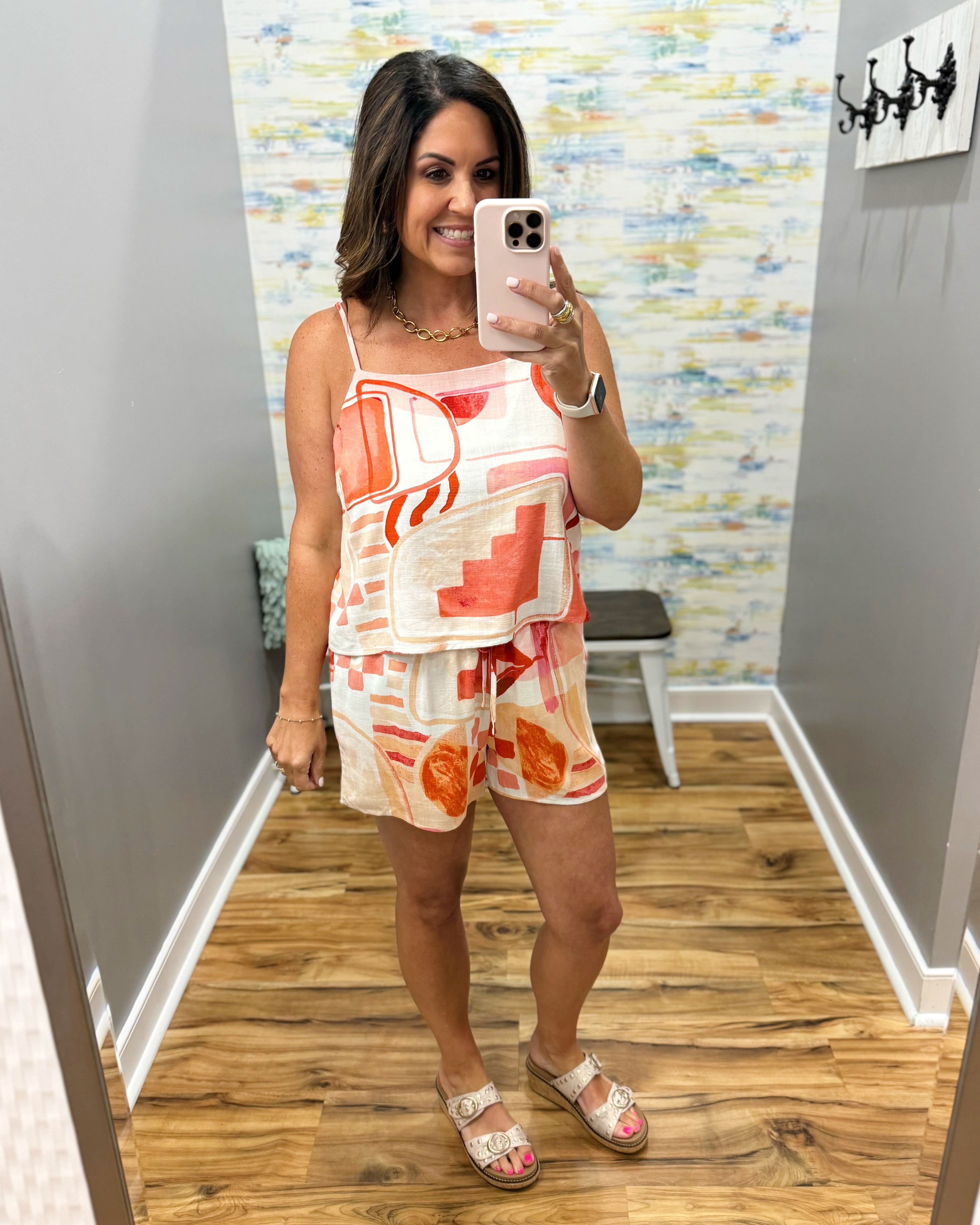 Woman taking a mirror selfie wearing a colorful dress in a room with patterned wallpaper.