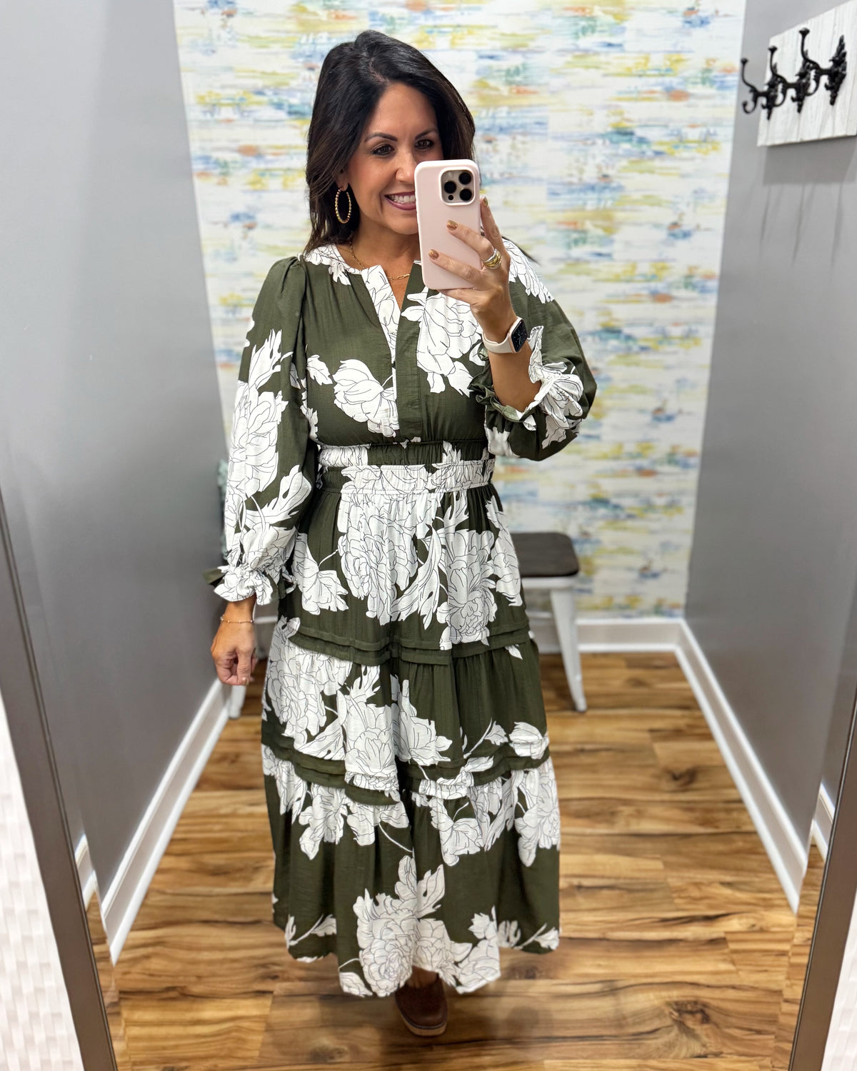 A woman takes a mirror selfie wearing a long-sleeve olive green maxi dress with a white floral print. The dress features a V-neckline, smock waist.