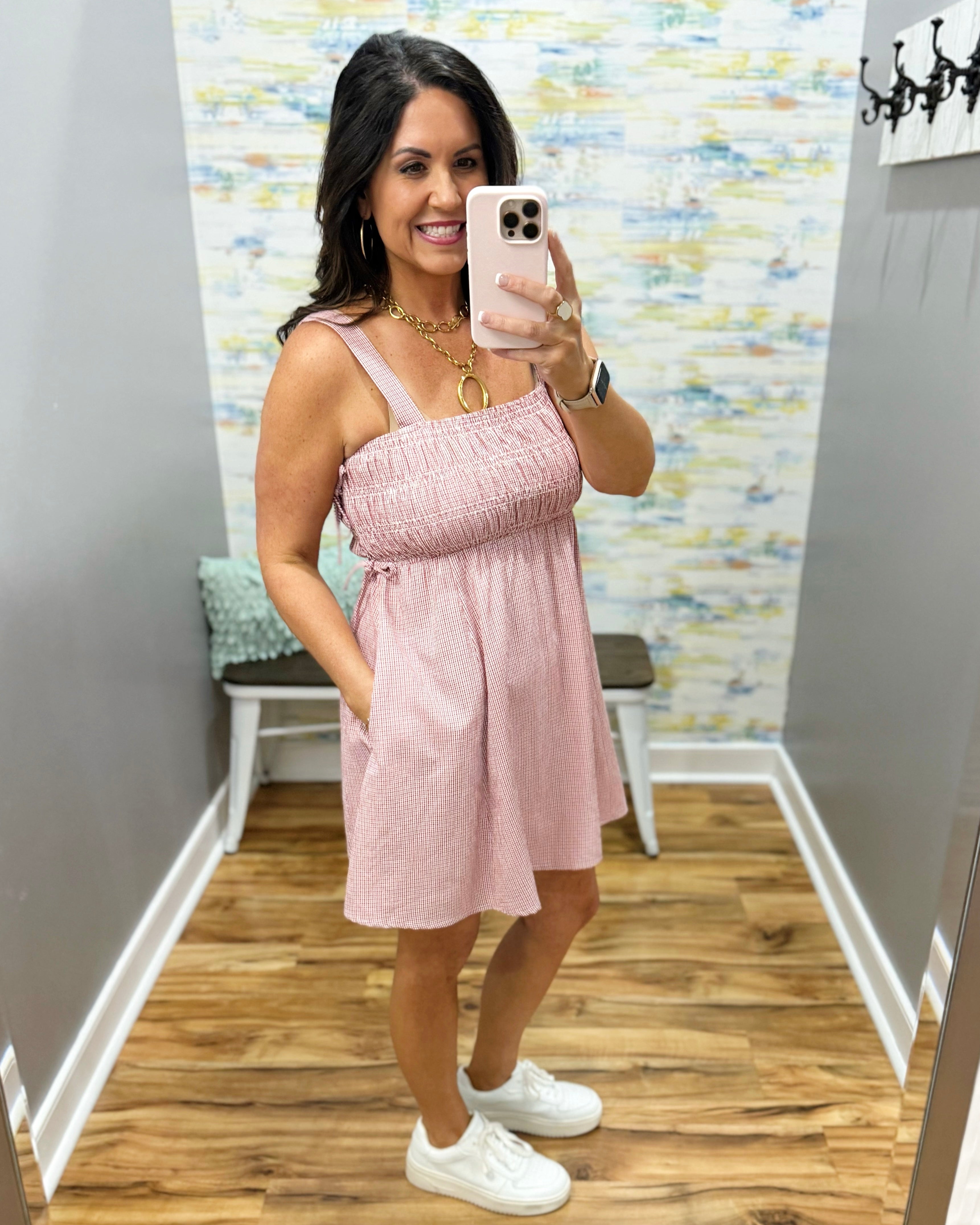 Woman taking a mirror selfie wearing a pink dress in a room with colorful wall art.