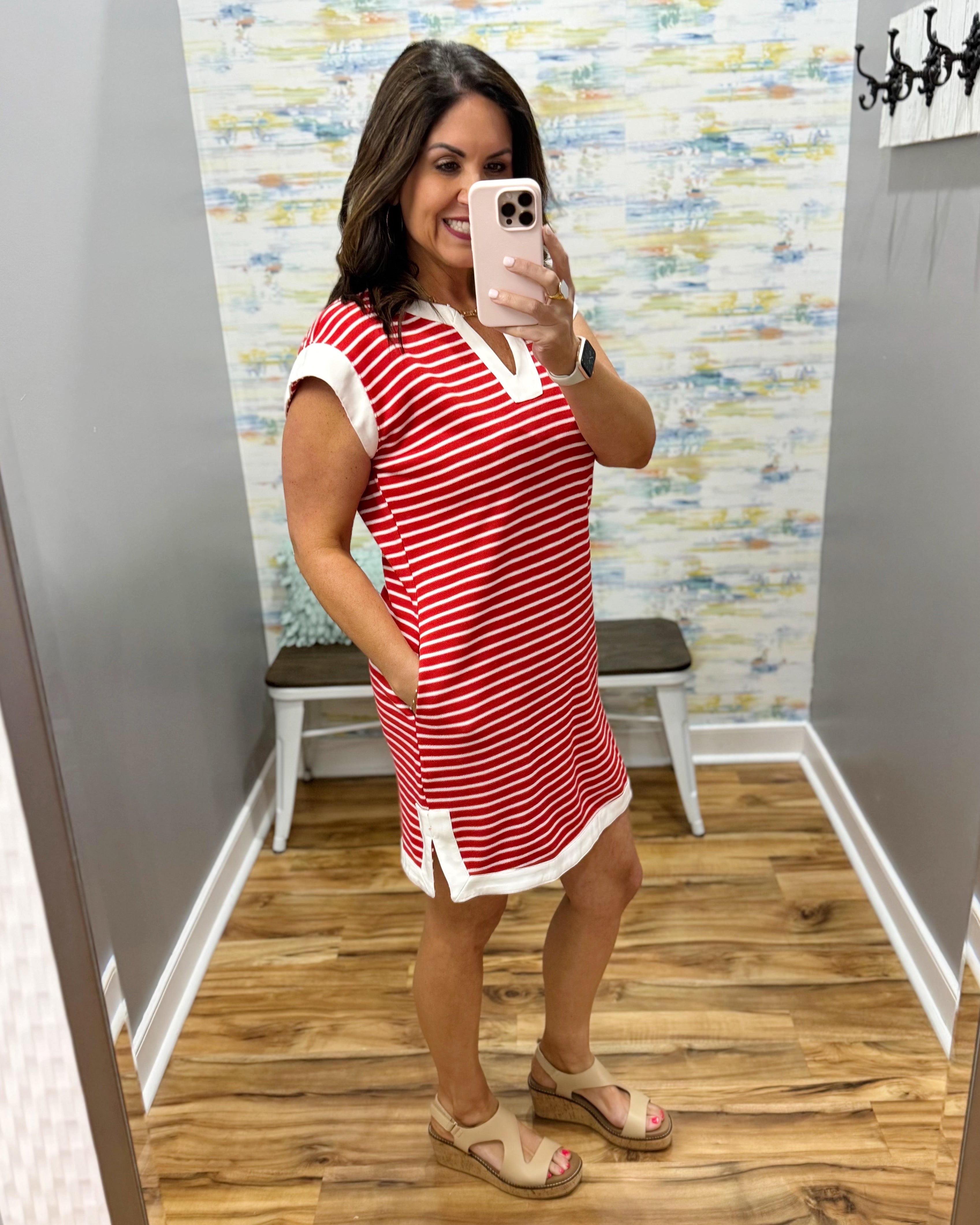 Woman taking a mirror selfie wearing a red and white striped dress in a room with a patterned wall.