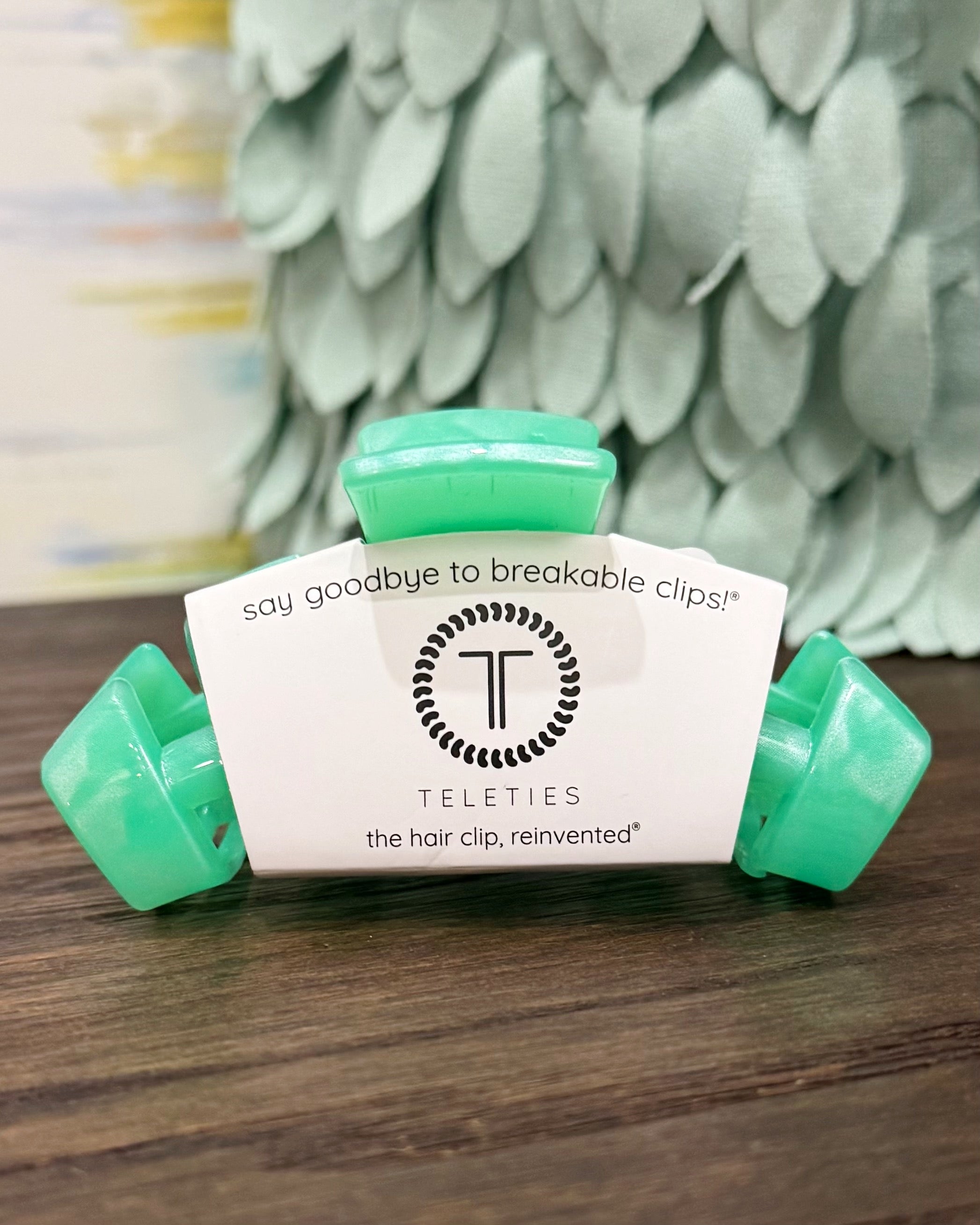 Teal hair clip with a white label on a wooden surface