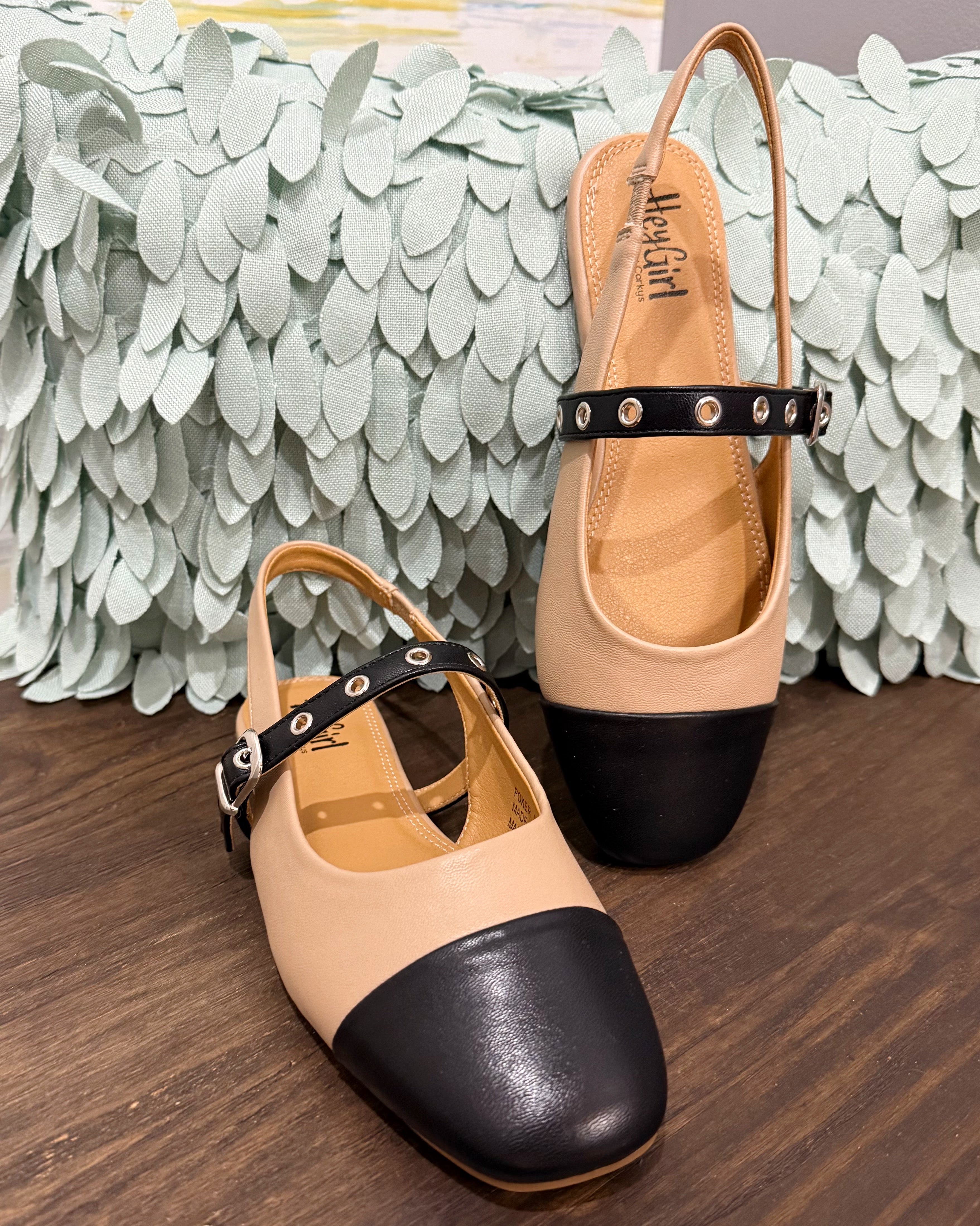 Pair of beige and black shoes with a strap on a wooden surface.