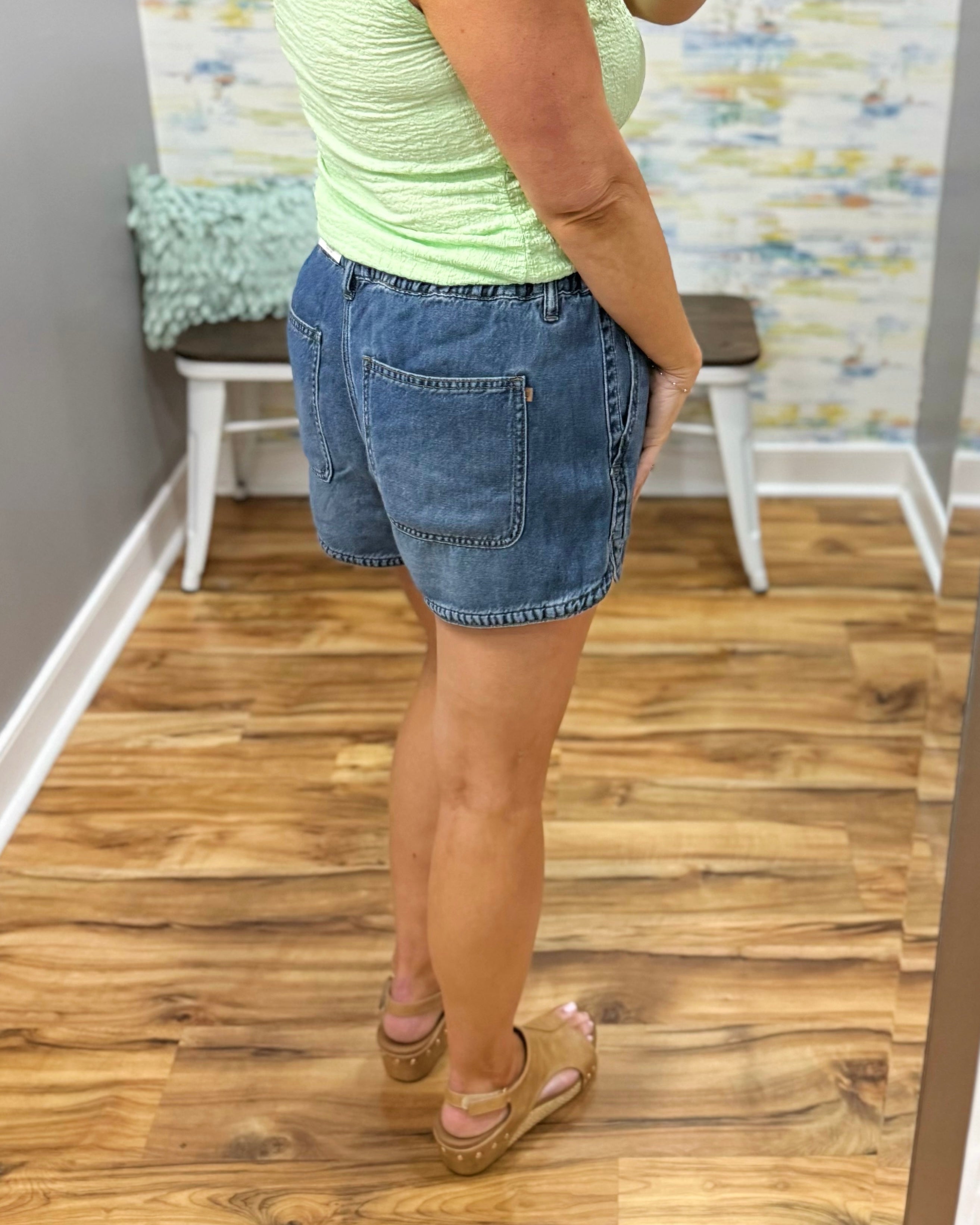 Person wearing a green top and blue denim shorts standing on a wooden floor.