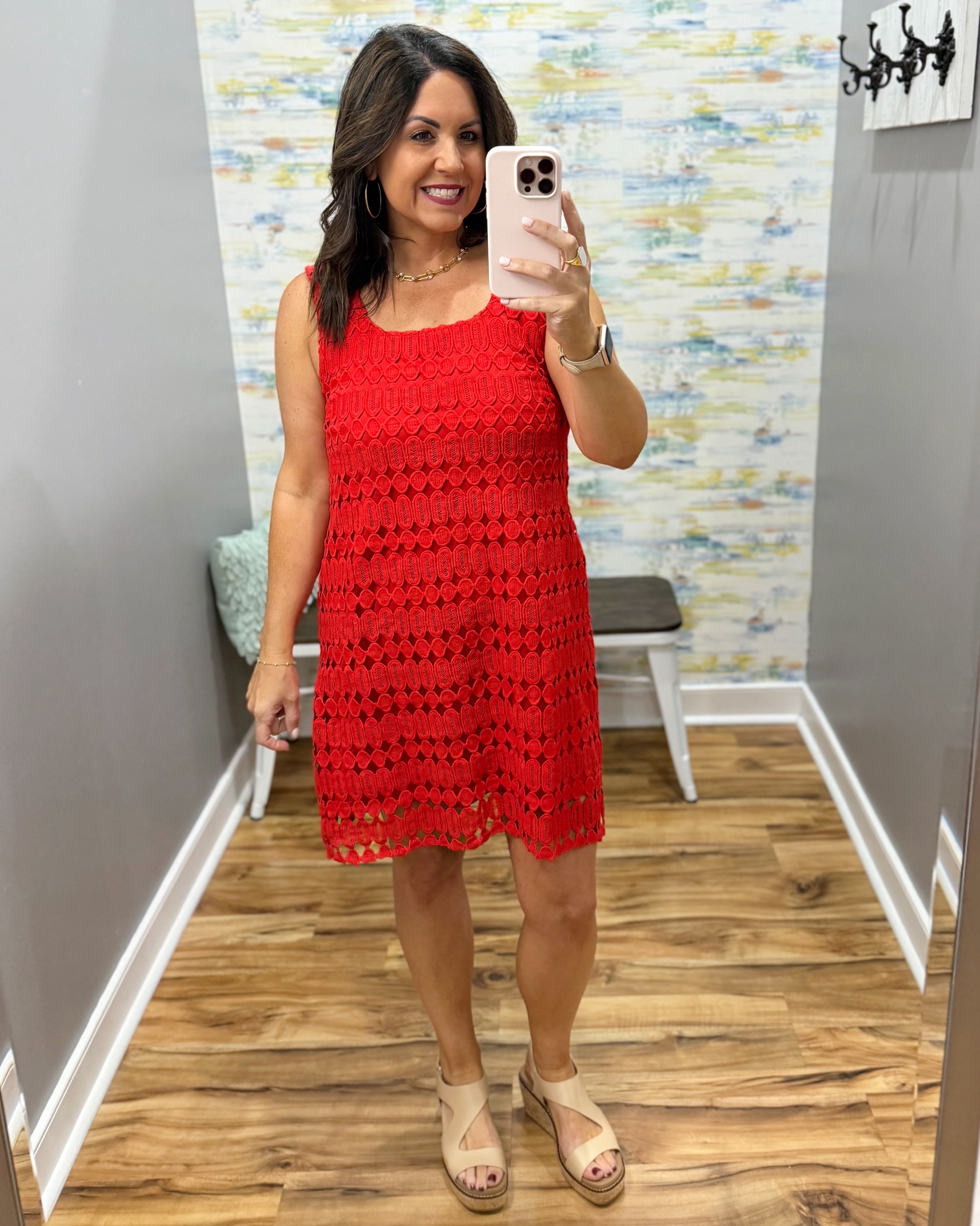 Woman taking a mirror selfie wearing a red crochet dress in a room with a colorful wall.