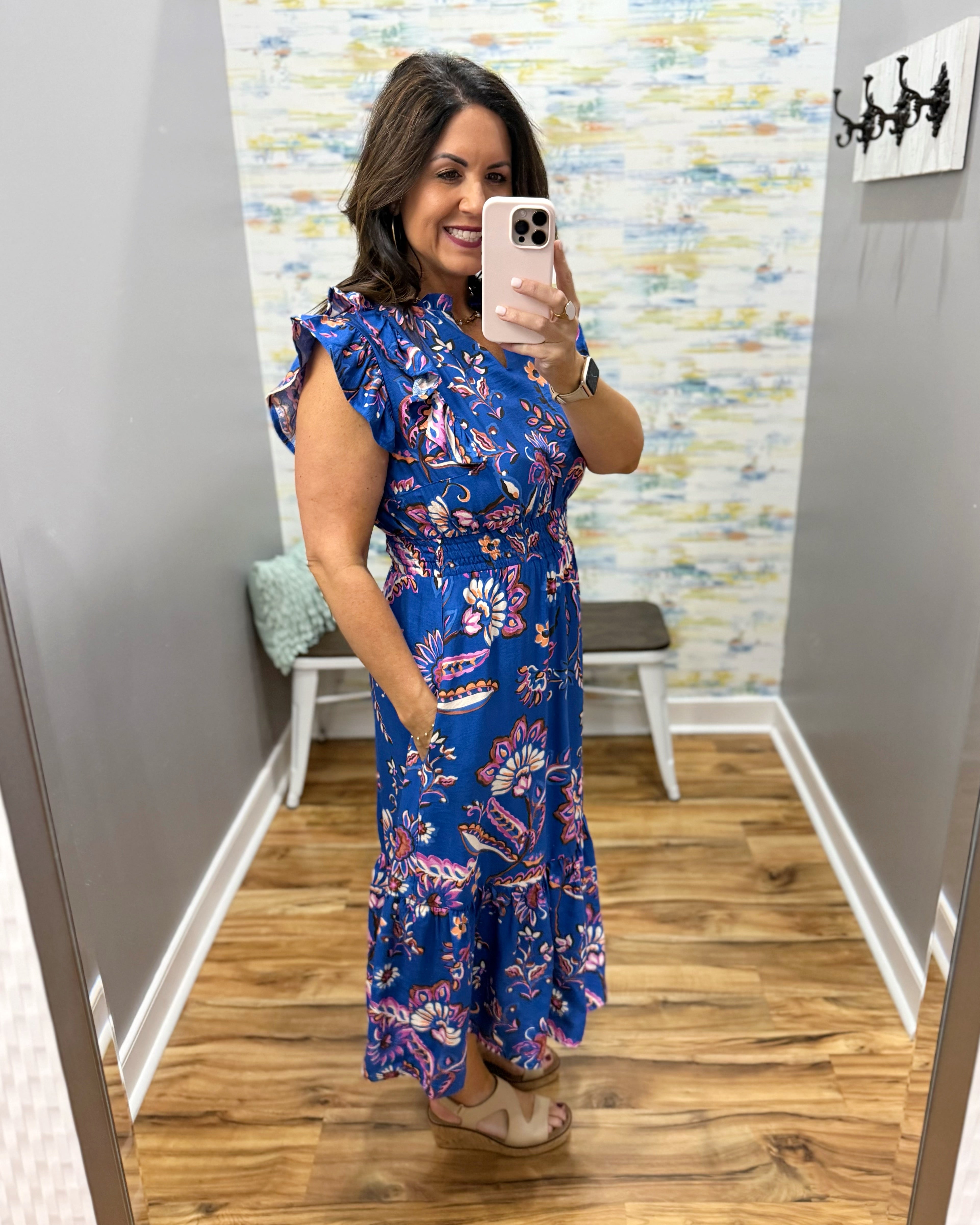 Woman taking a mirror selfie wearing a blue floral dress in a room with a colorful wall.