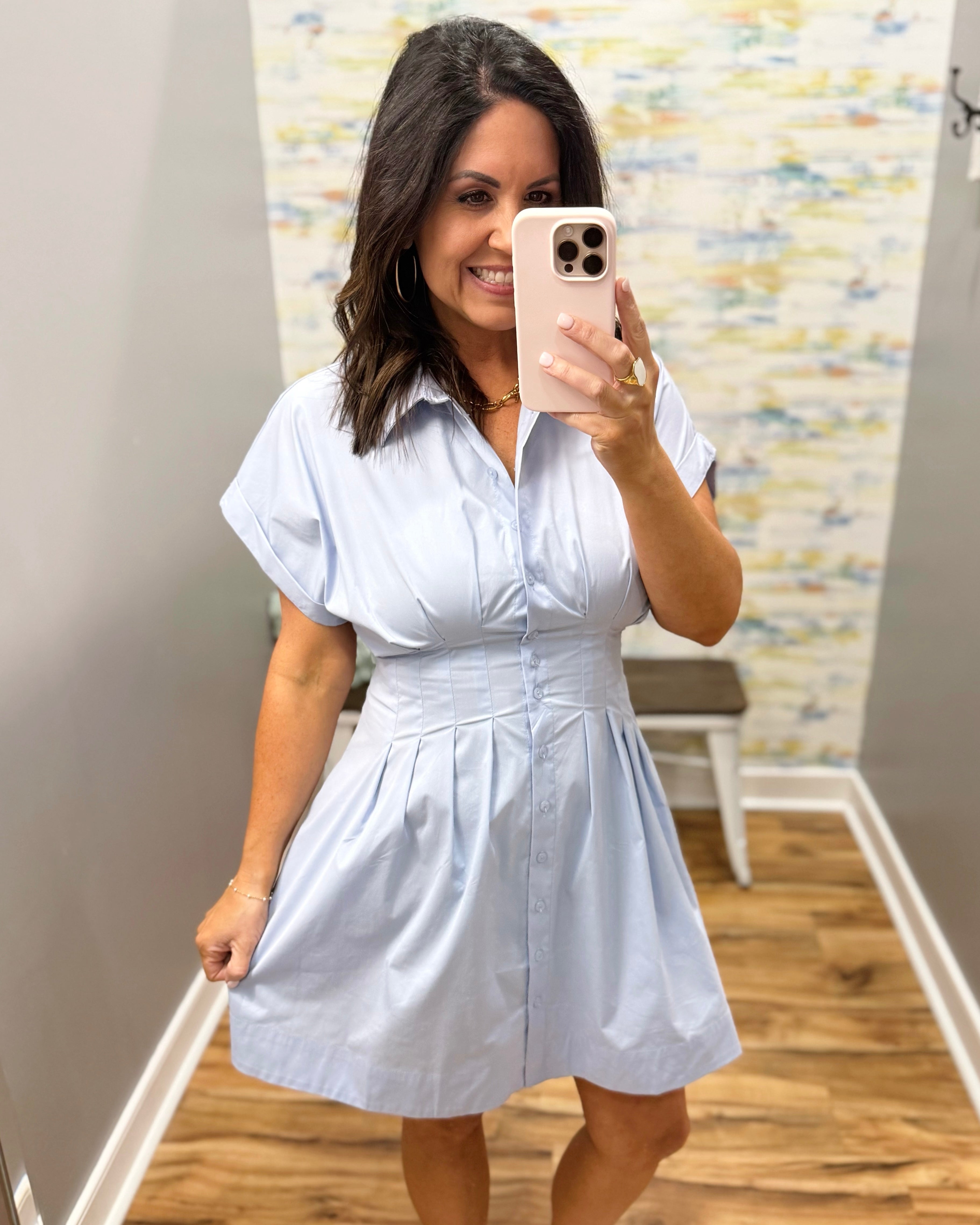 Woman taking a mirror selfie wearing a white dress in a room with a colorful wall.