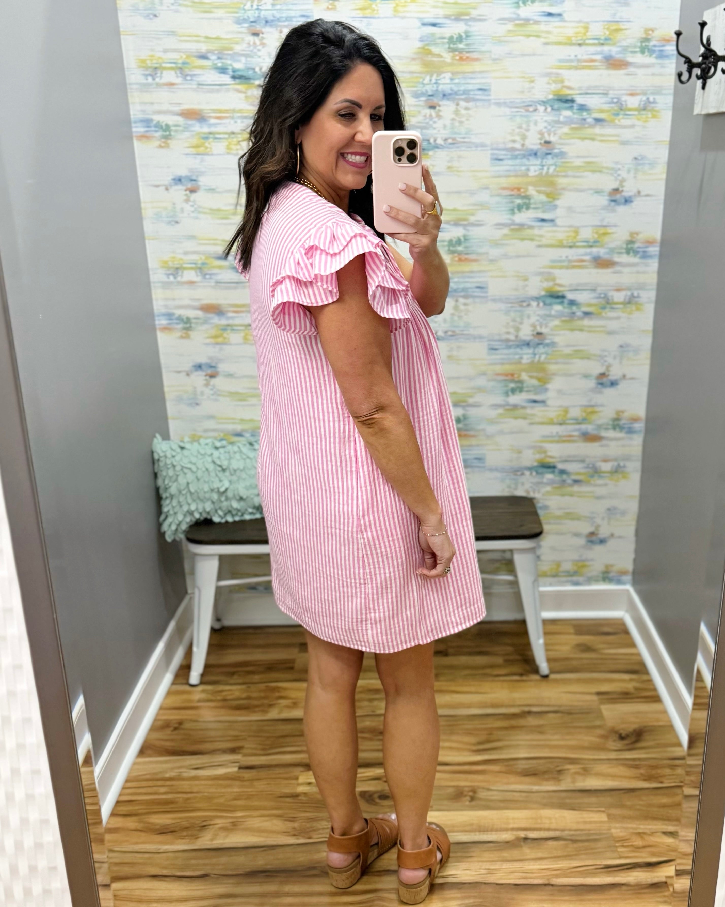 Woman wearing a pink dress taking a mirror selfie in a store.
