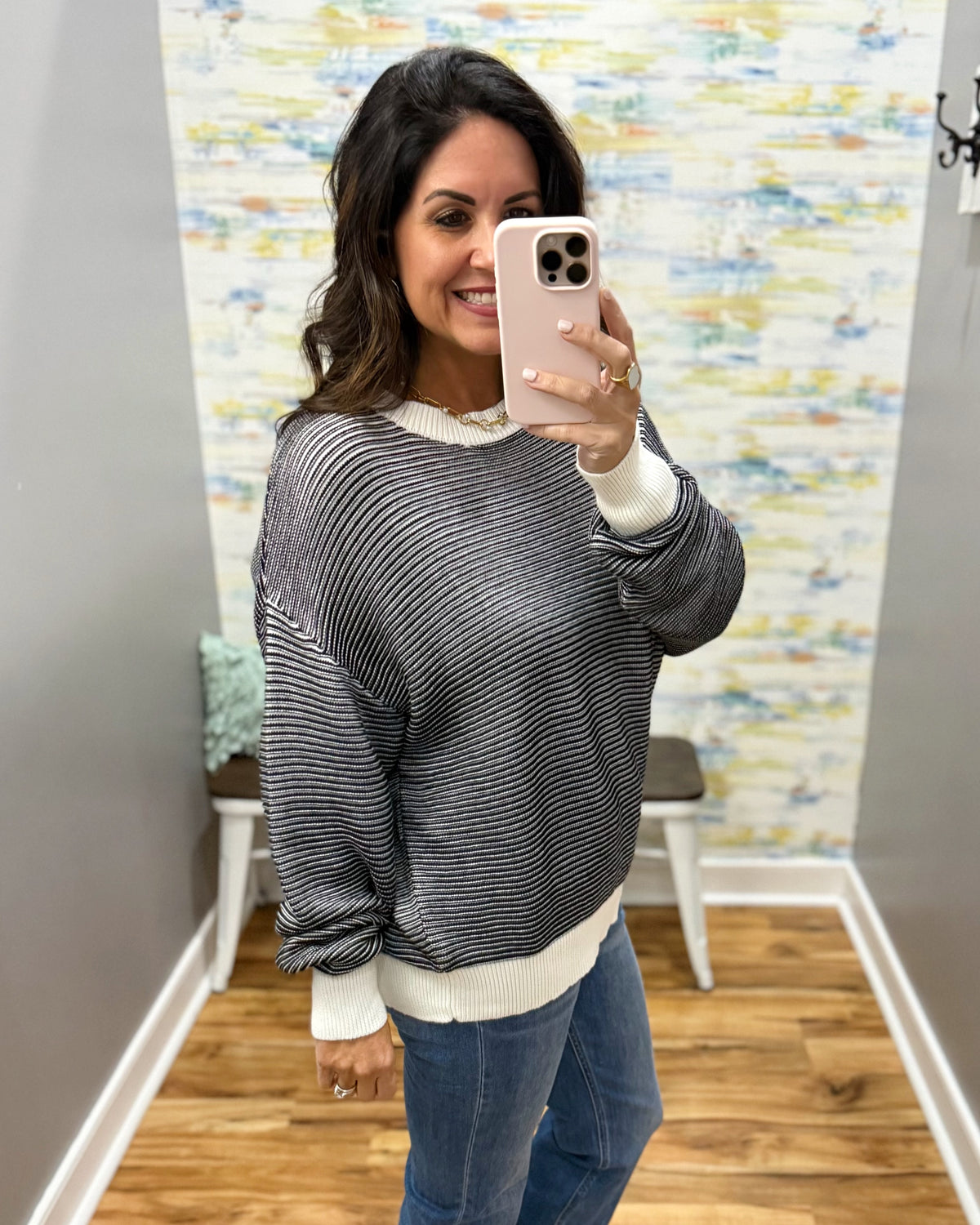 A woman takes a mirror selfie wearing a black and white horizontally striped long-sleeve knit sweater with white ribbed cuffs and hem, paired with blue jeans.