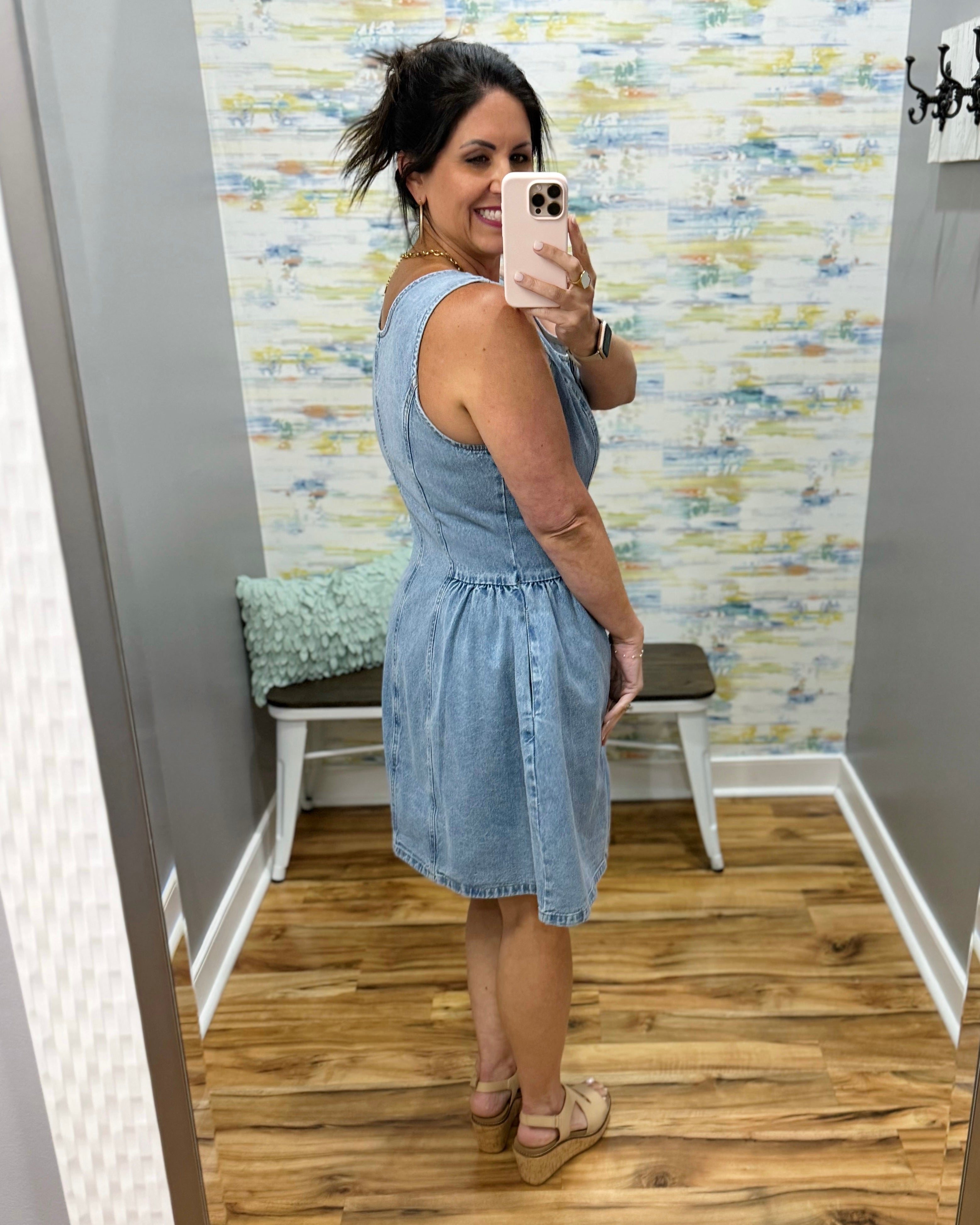 Woman taking a mirror selfie wearing a denim dress in a room with a colorful wall.