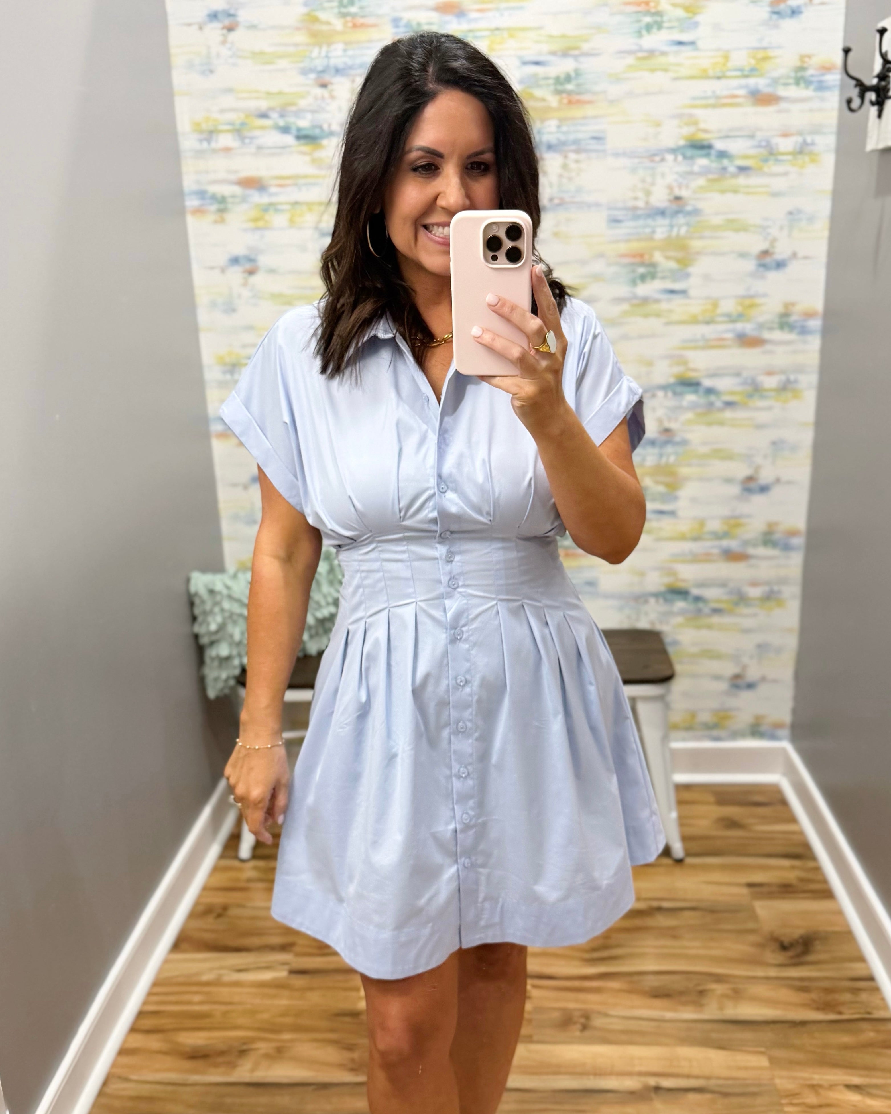 Woman taking a mirror selfie wearing a light blue dress in a room with a patterned wall.