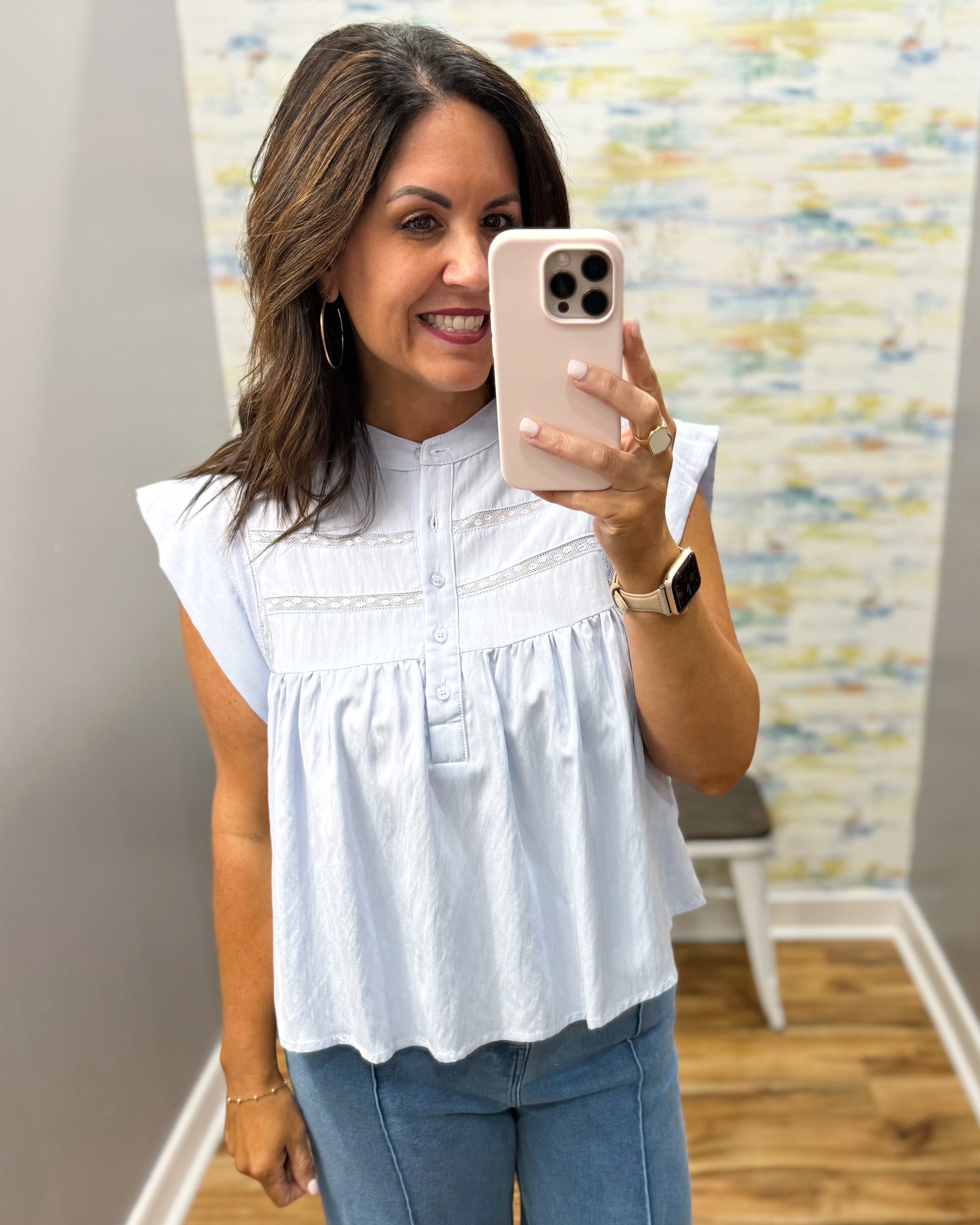 Woman taking a mirror selfie wearing a white blouse and blue jeans in a room with a colorful wall.