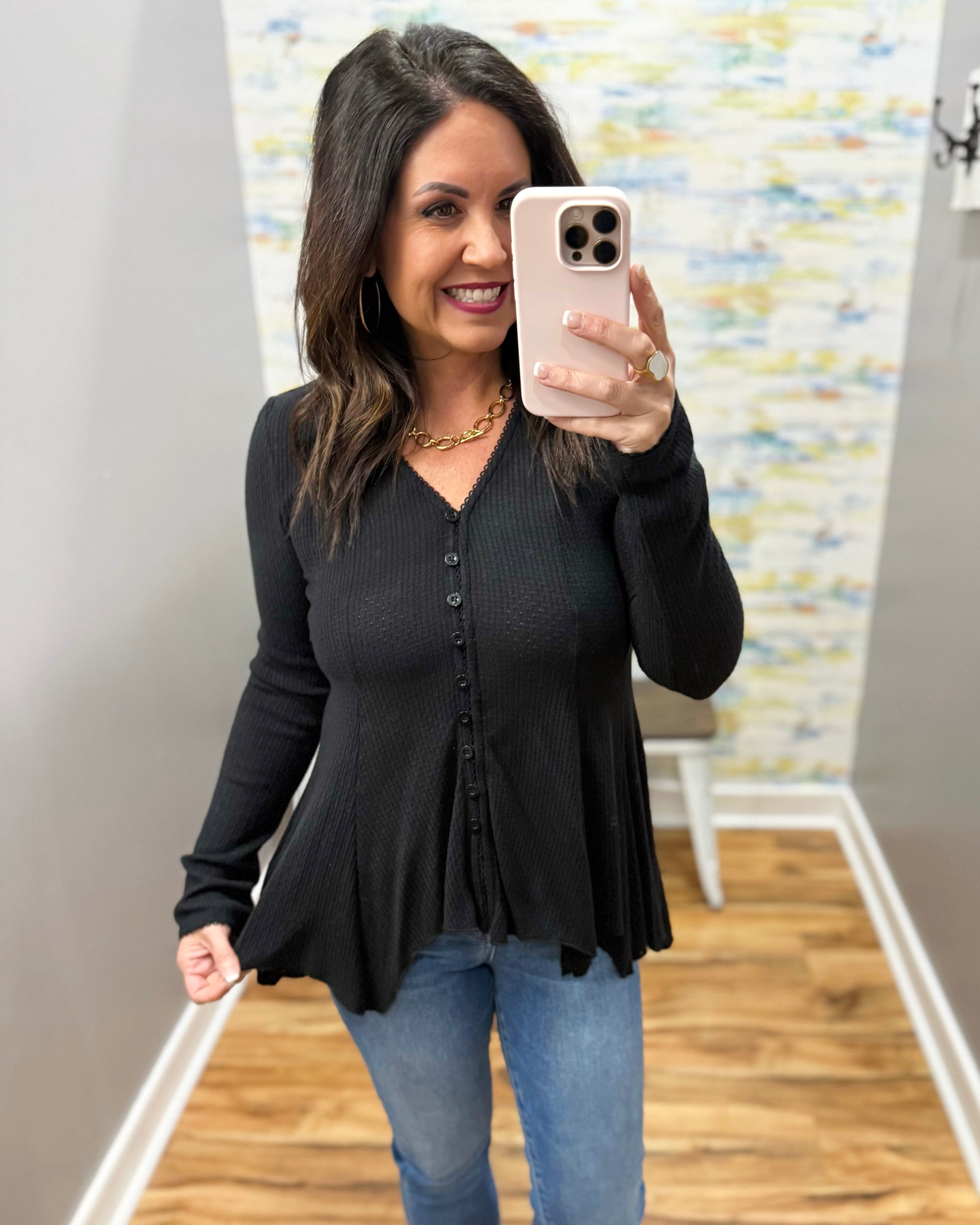 Woman taking a mirror selfie wearing a black long-sleeve top and blue jeans.