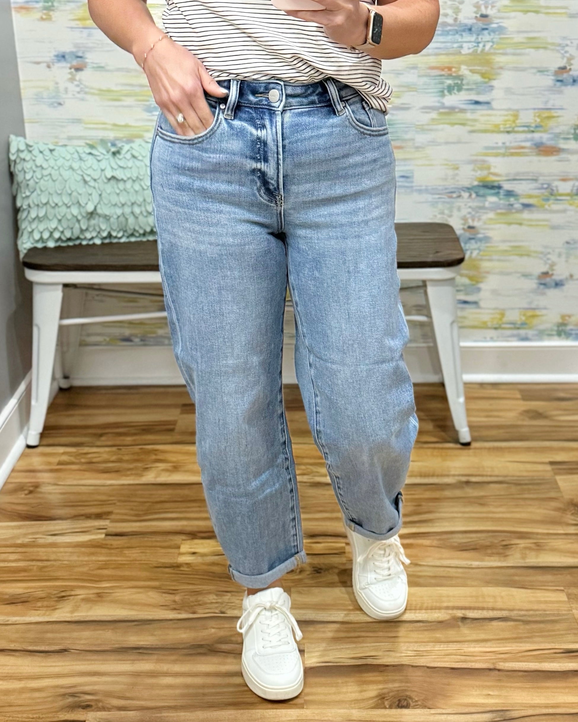 Person wearing light blue jeans and white sneakers in a room with a wooden floor and colorful wall.