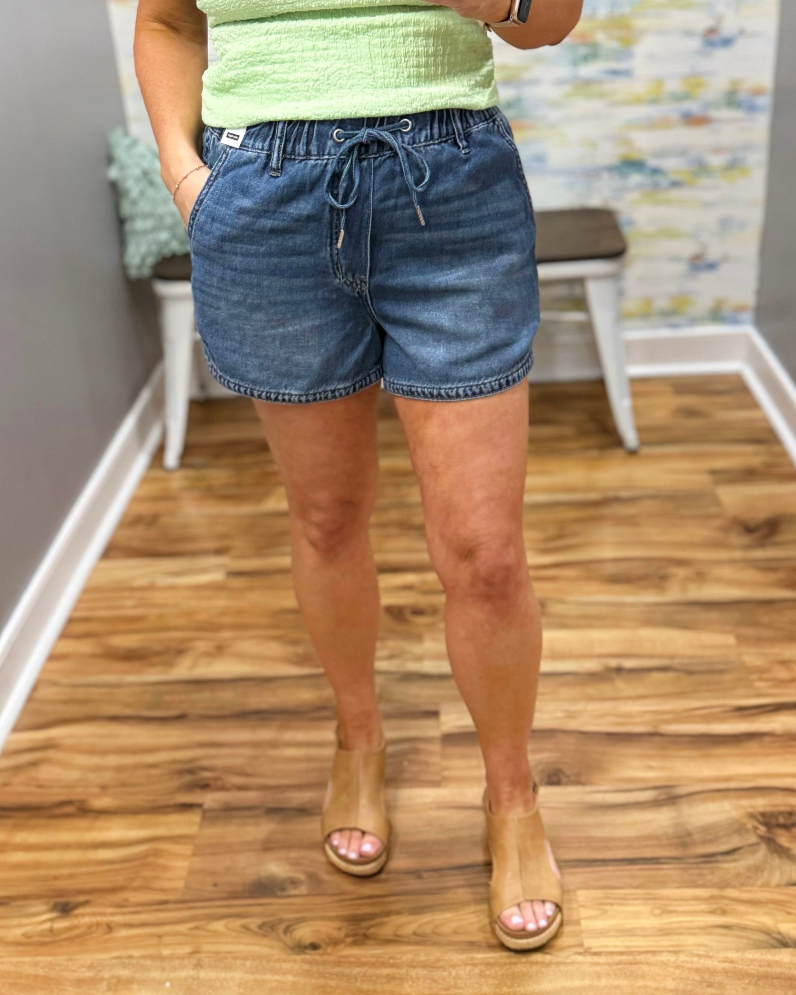 Person wearing blue denim shorts and a green top on a wooden floor.
