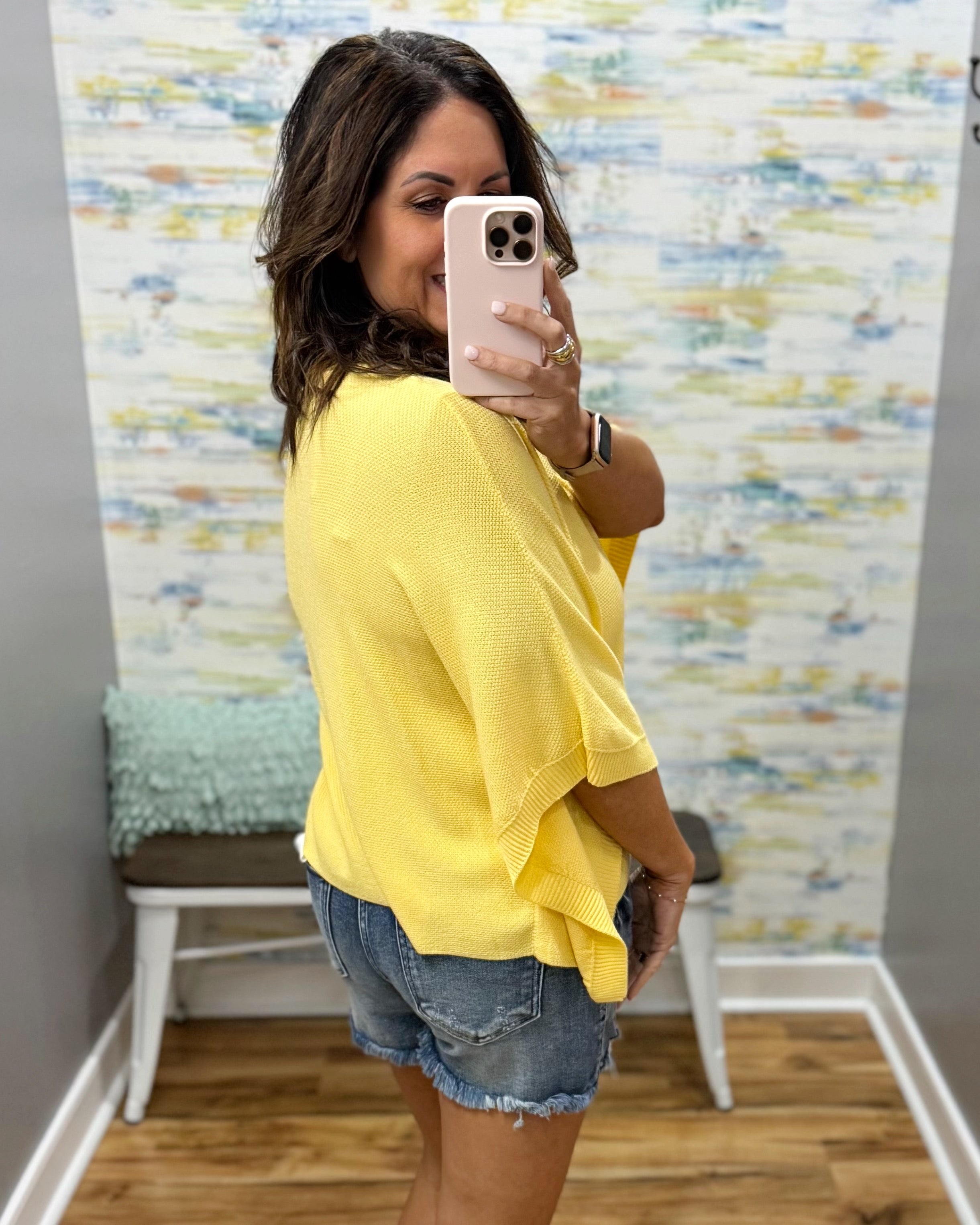 woman wearing a yellow dolman sleeve top with denim shorts.