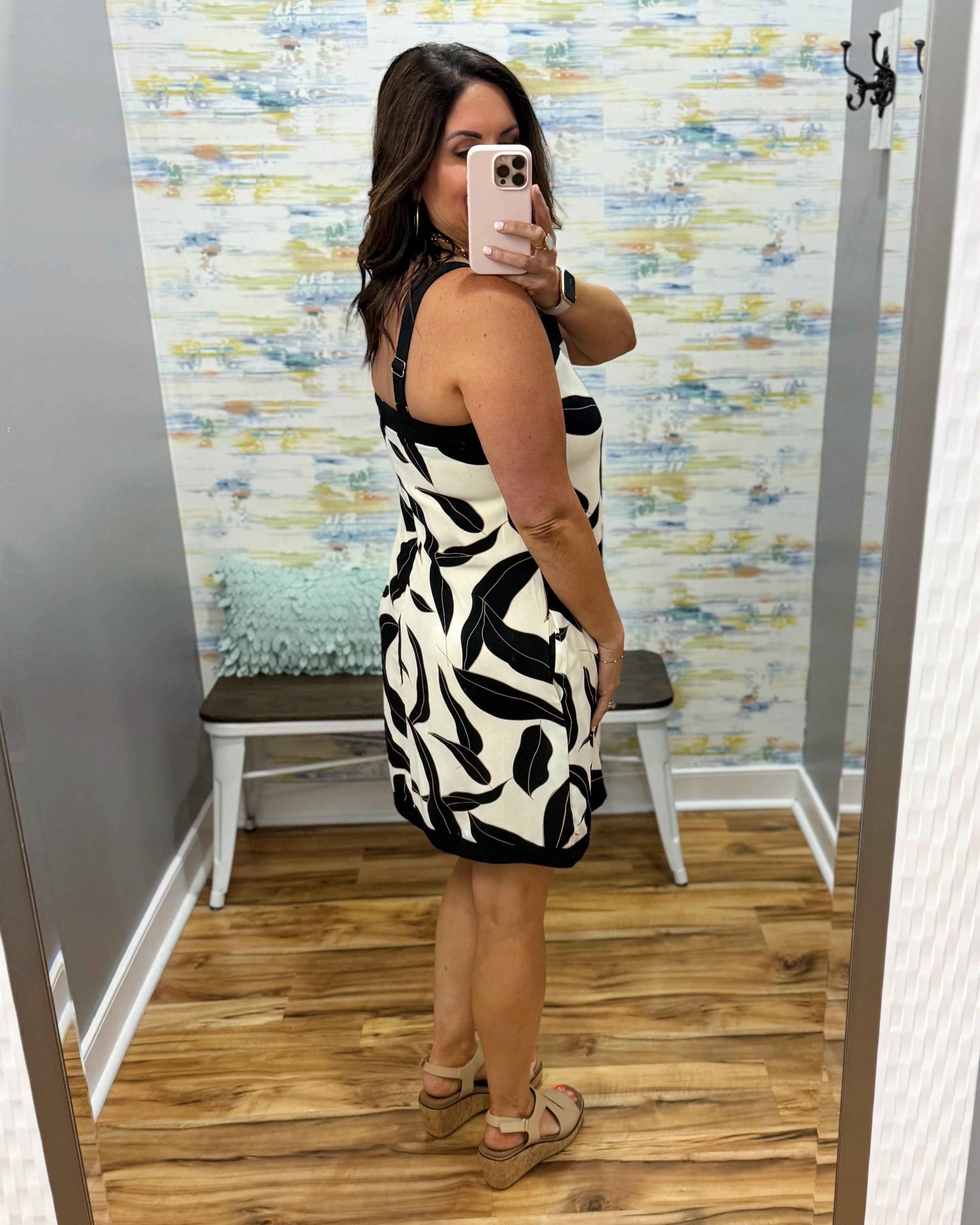 Woman taking a mirror selfie wearing a black and white patterned dress in a fitting room.
