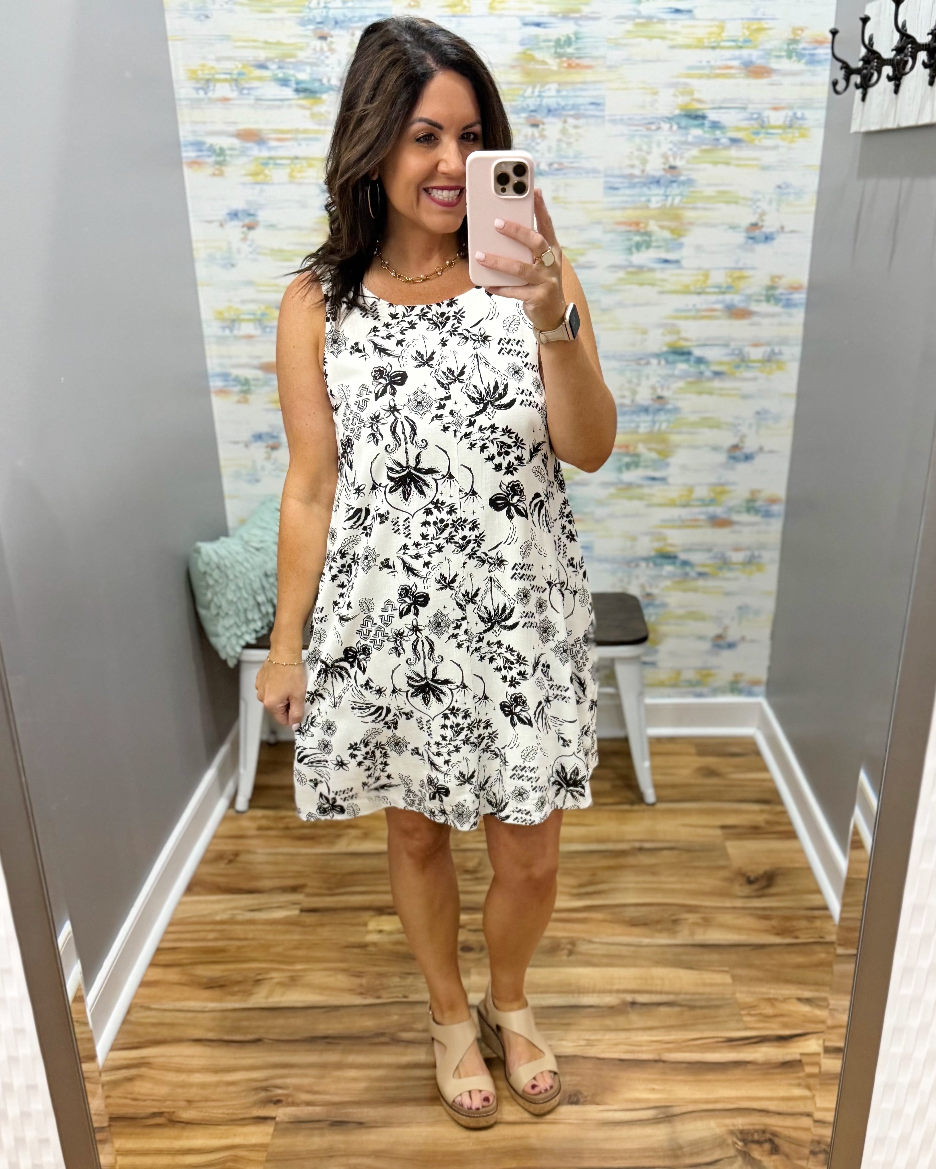 Woman wearing a white dress with black floral pattern in a fitting room.