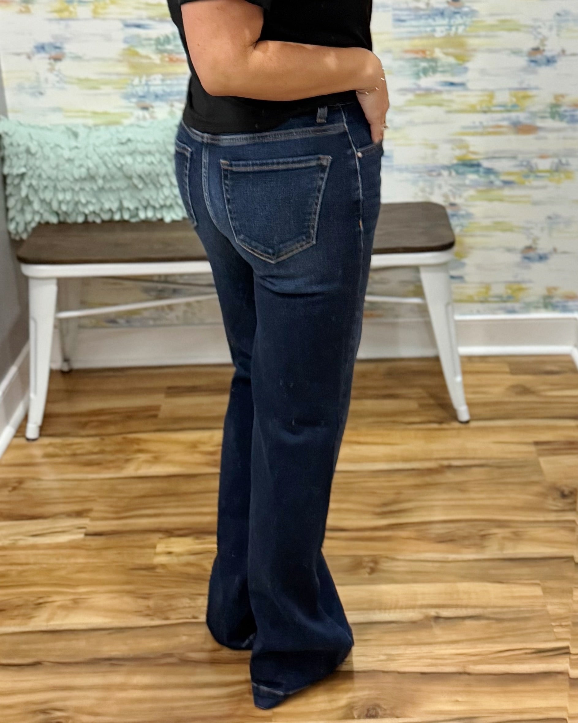 Person wearing dark blue jeans standing on a wooden floor with a colorful wall in the background.