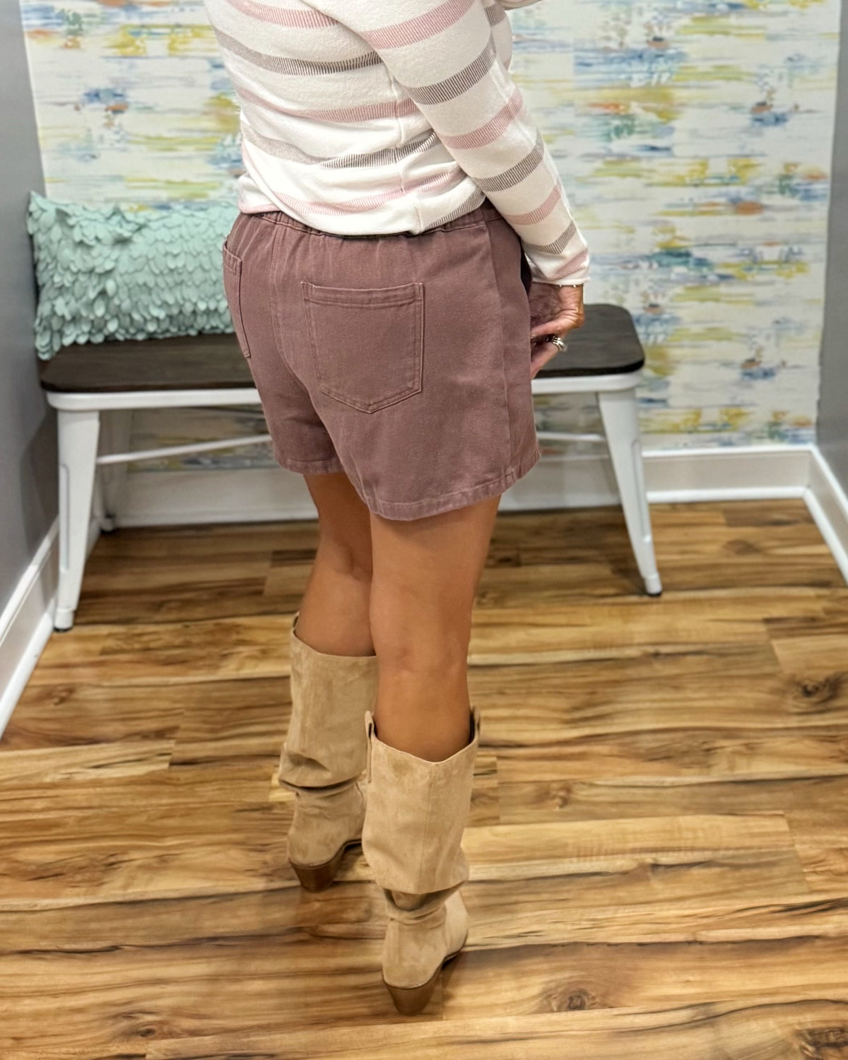 A person wearing a chestnut color wrap-style mini skirt with a single button closure, paired with a pink and white striped long-sleeve top and Corkys City Slicker boots in Sand Faux Suede.