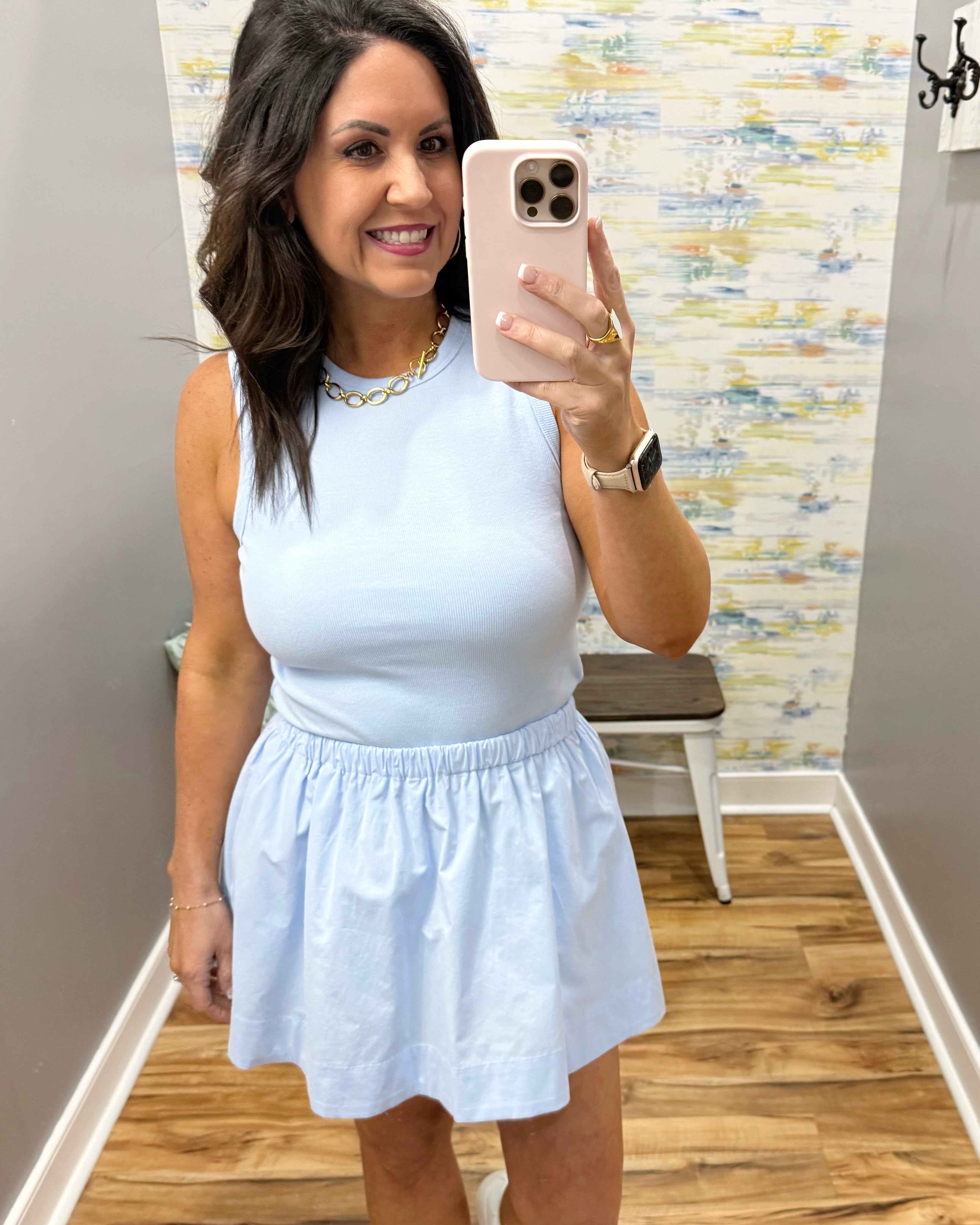 Woman taking a mirror selfie wearing a light blue dress in a room with a patterned wall.