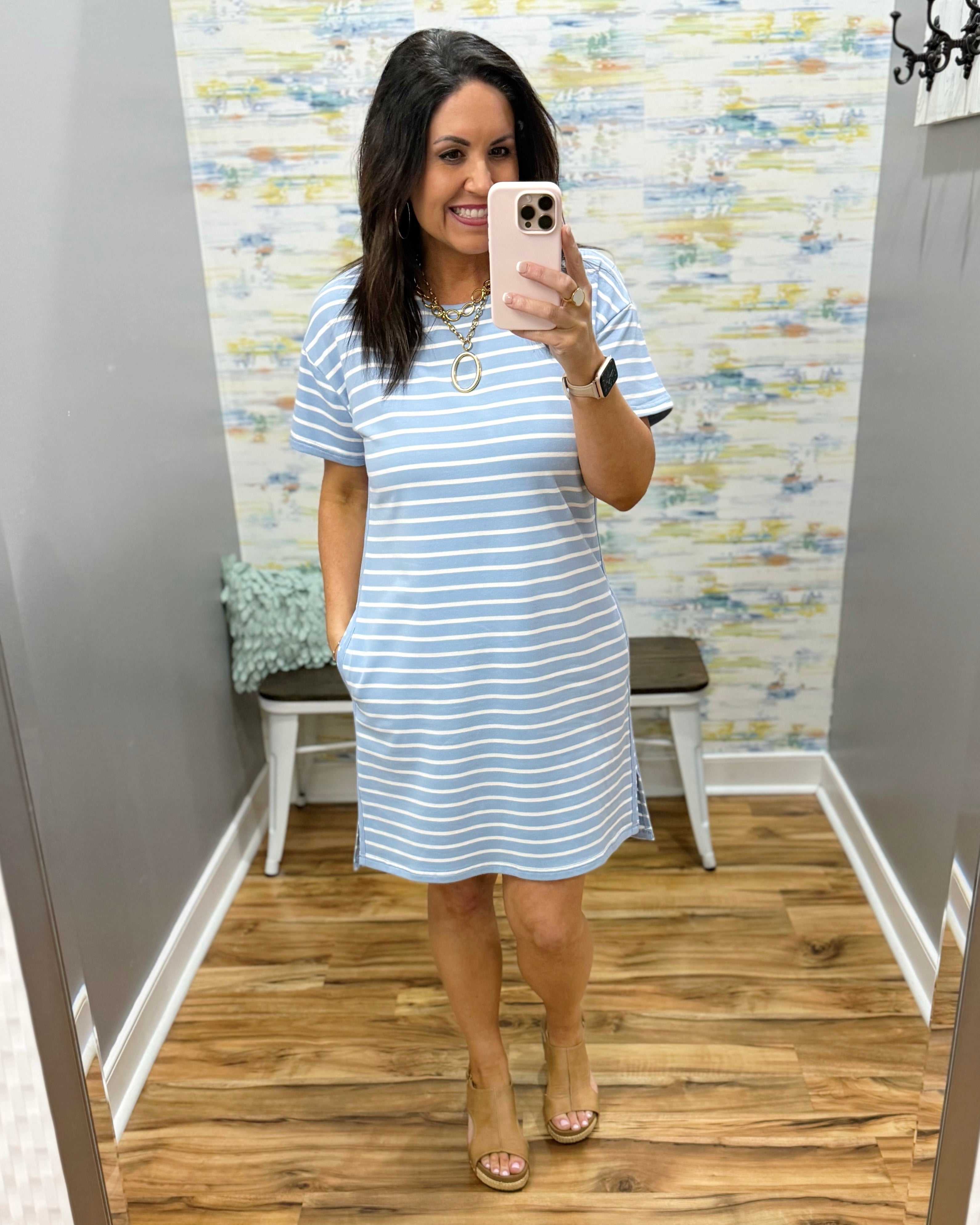 Woman wearing a blue and white striped dress in a room with patterned wallpaper.