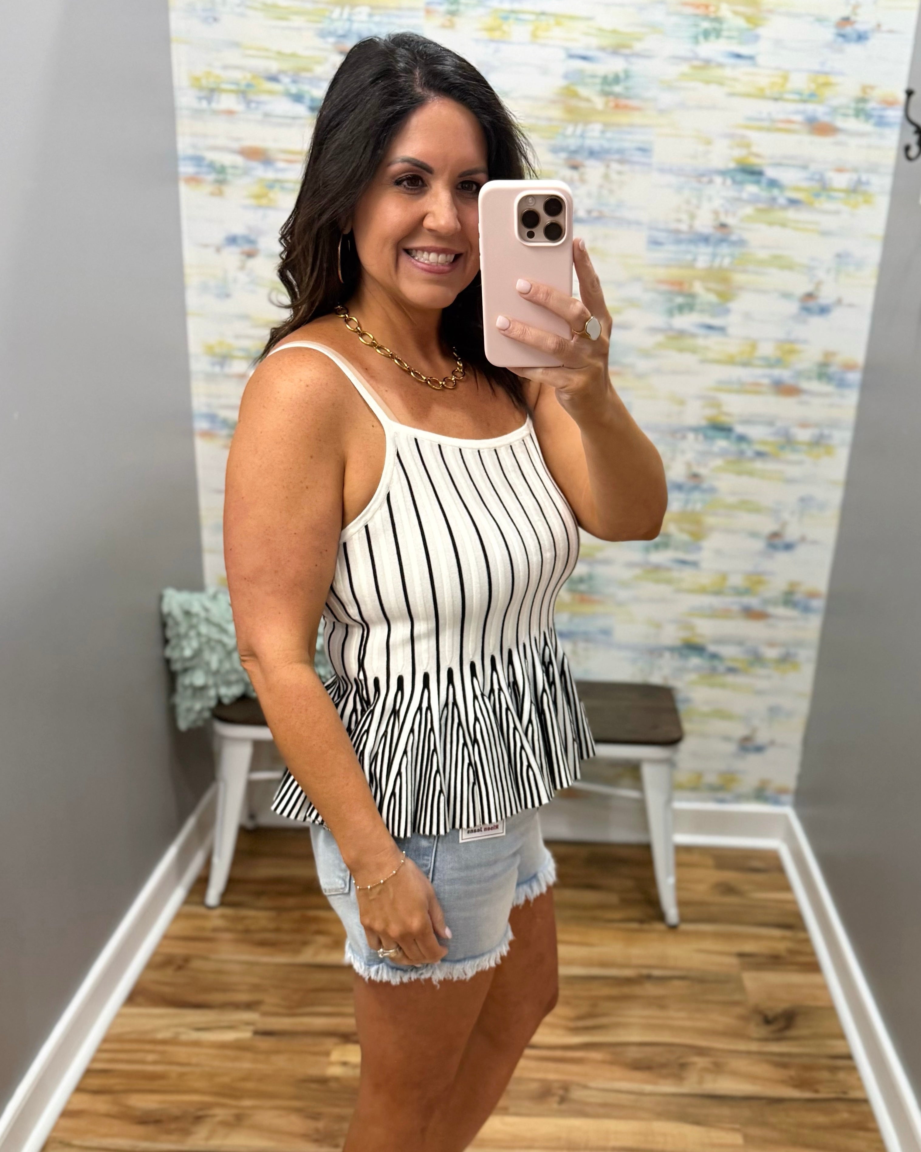 Woman taking a mirror selfie wearing a black and white striped top and denim shorts in a room with colorful wall art.