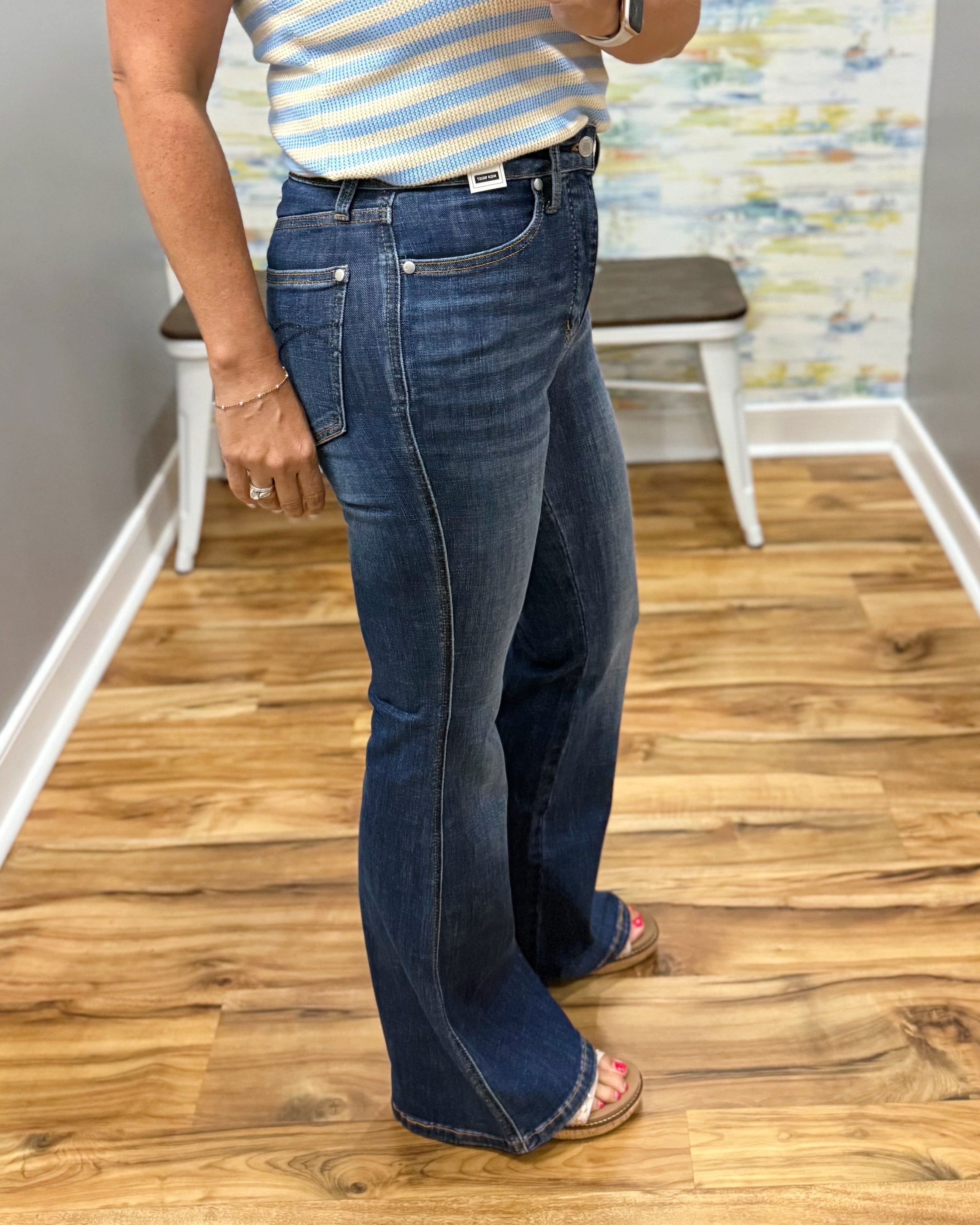 Person wearing blue jeans and a striped shirt on a wooden floor.
