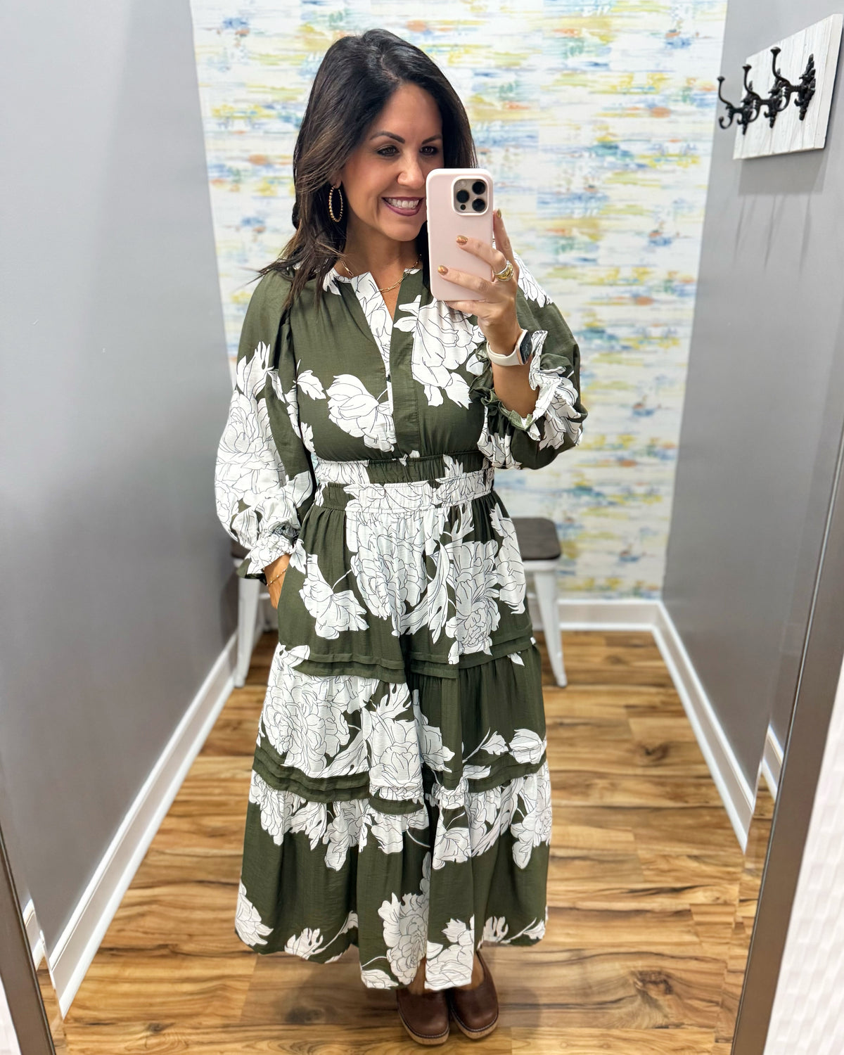 A woman takes a mirror selfie wearing a long-sleeve olive green maxi dress with a white floral print. The dress features a V-neckline, smock waist.