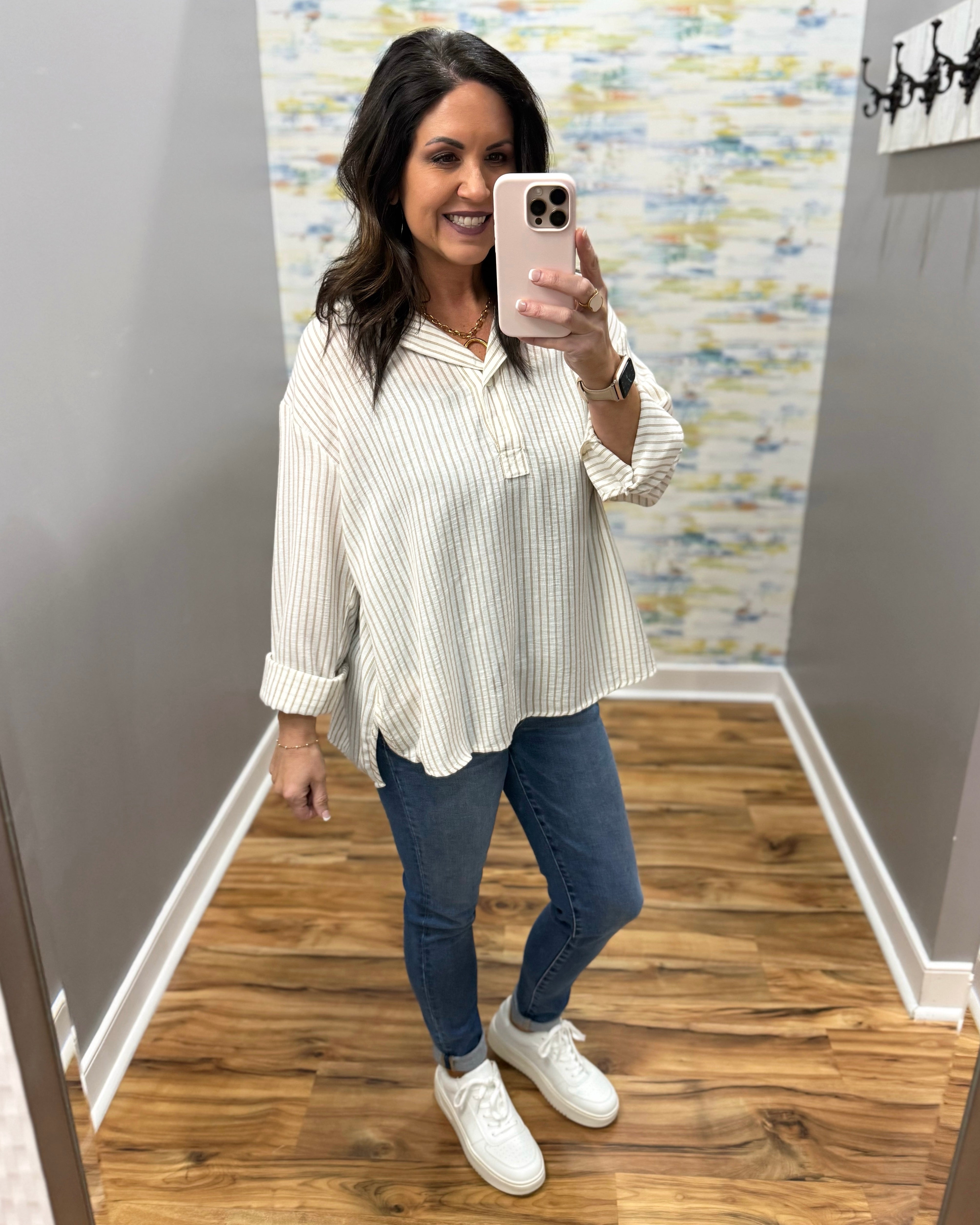 woman wearing a stripe blouse in mocha and white with skinny jeans and white sneakers.