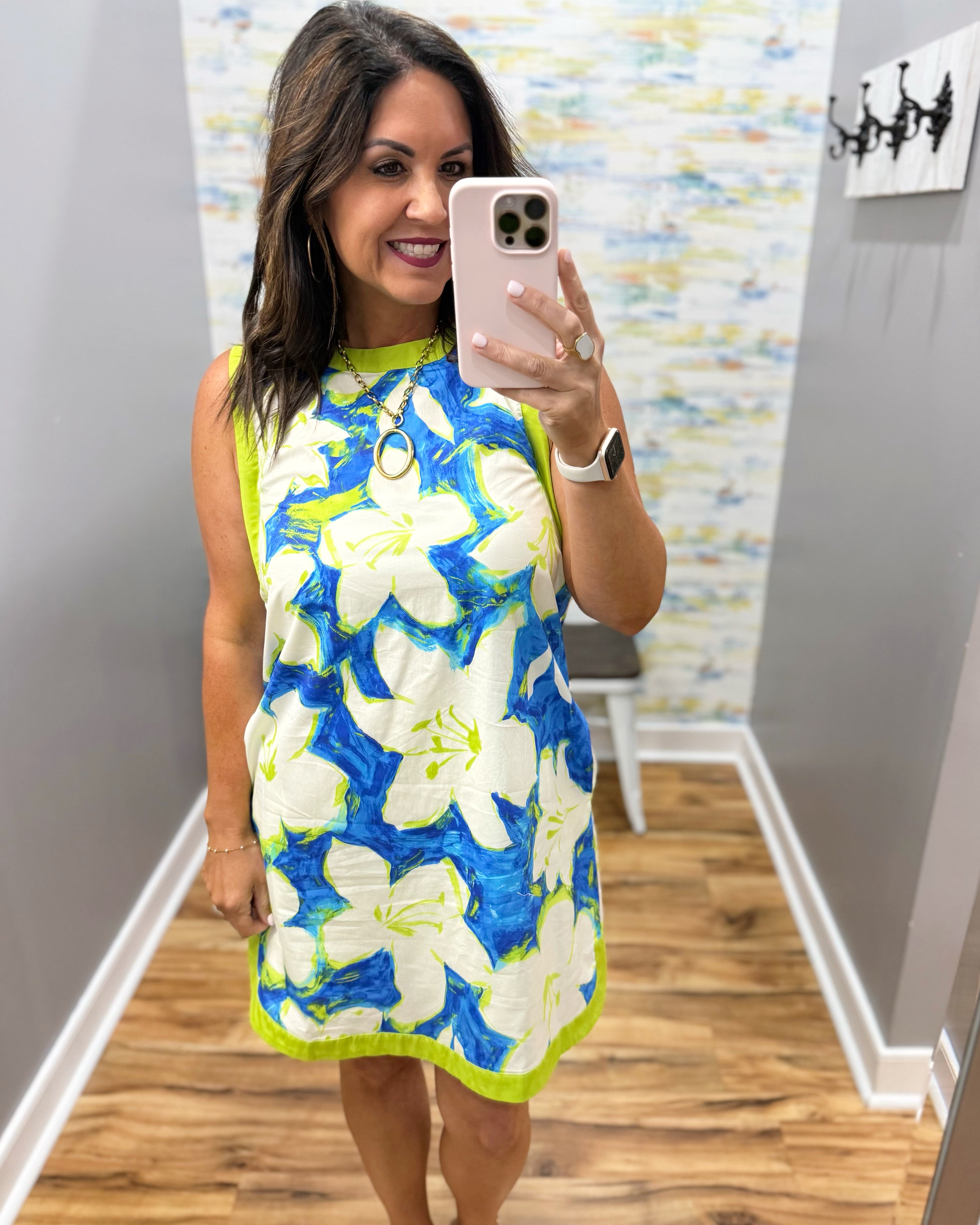 Woman taking a mirror selfie wearing a floral dress in a room with a patterned wall.