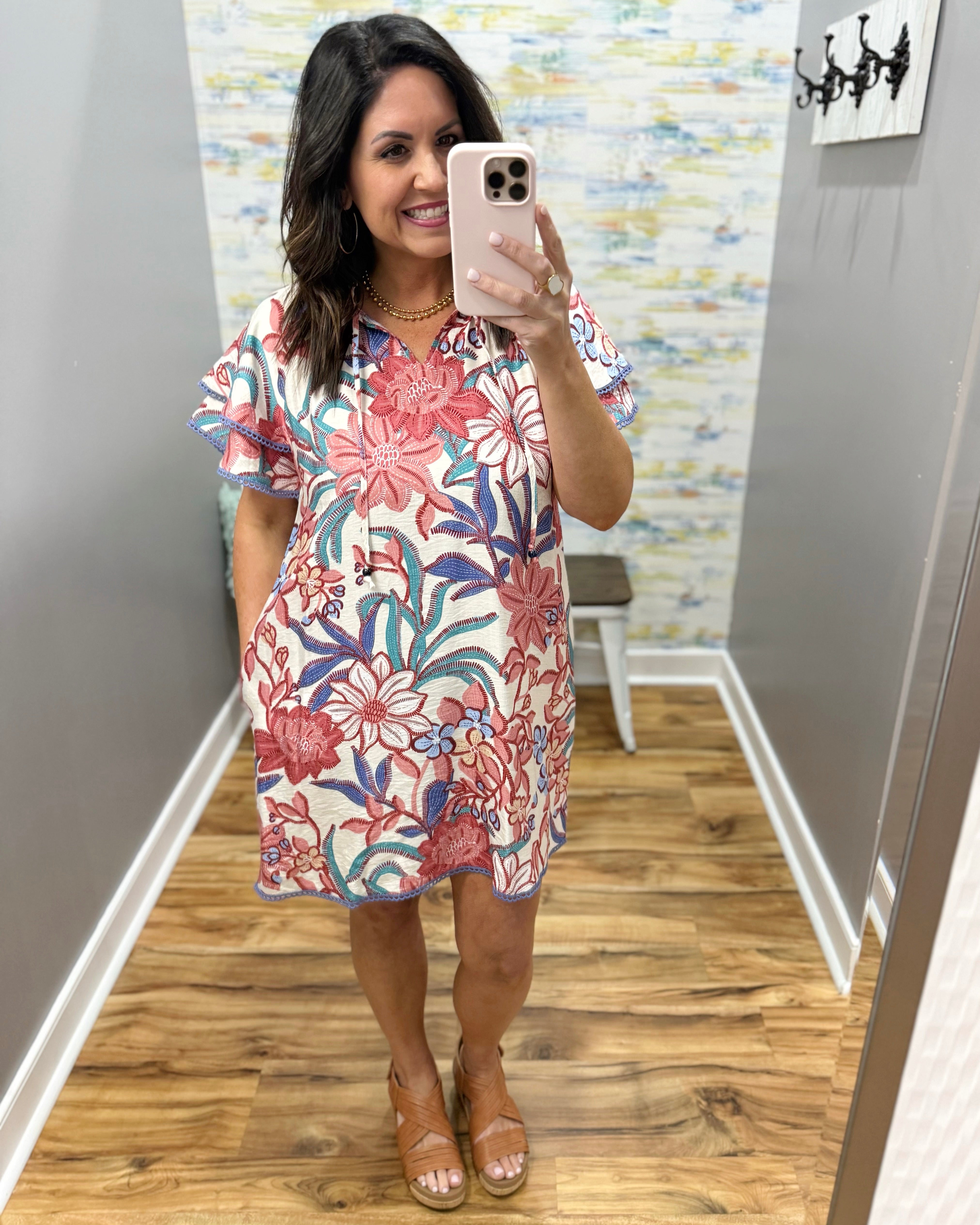 Woman taking a mirror selfie wearing a floral dress in a room with a colorful wall.